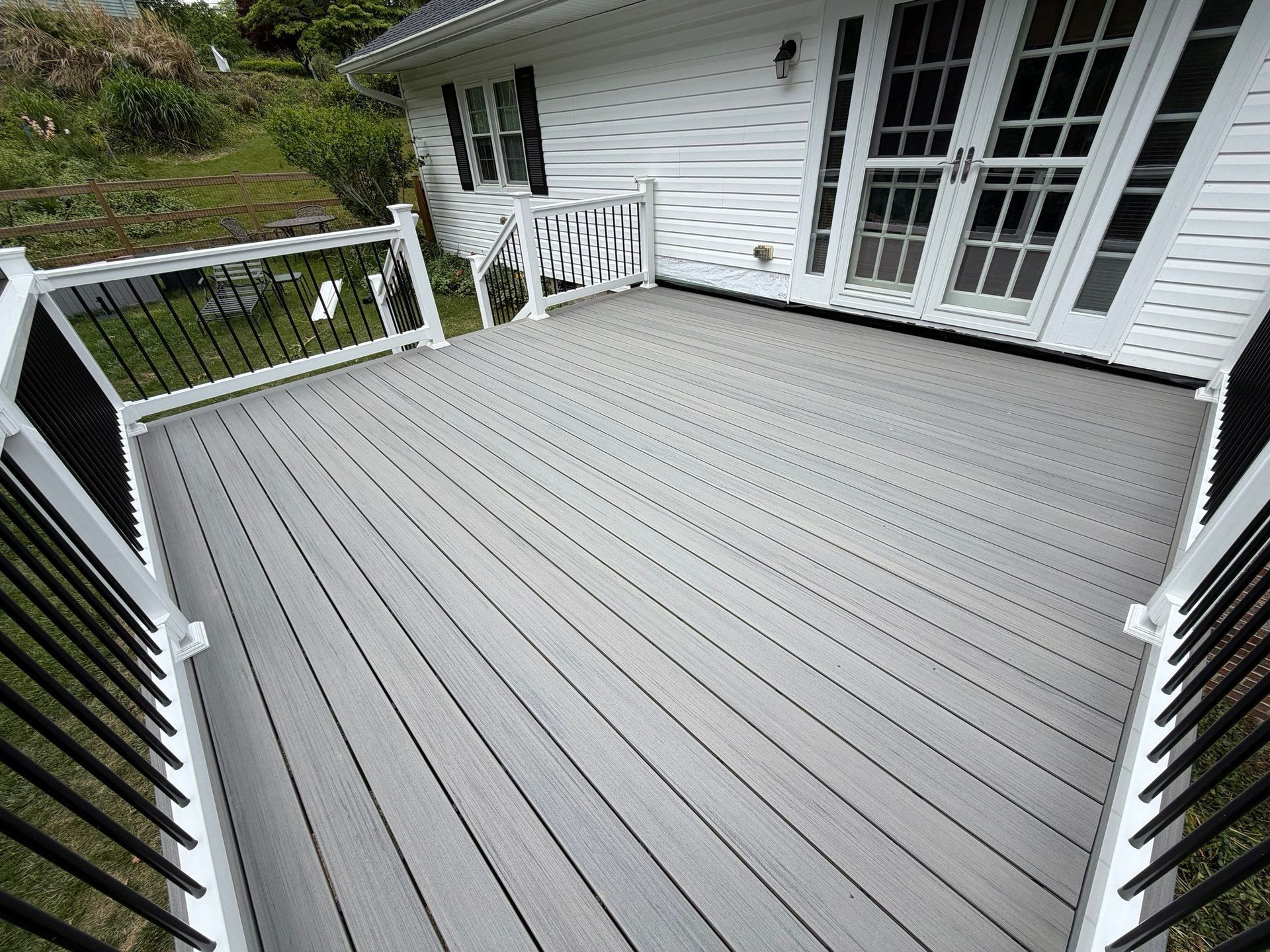 Gray wooden deck with white railings and French doors on a house