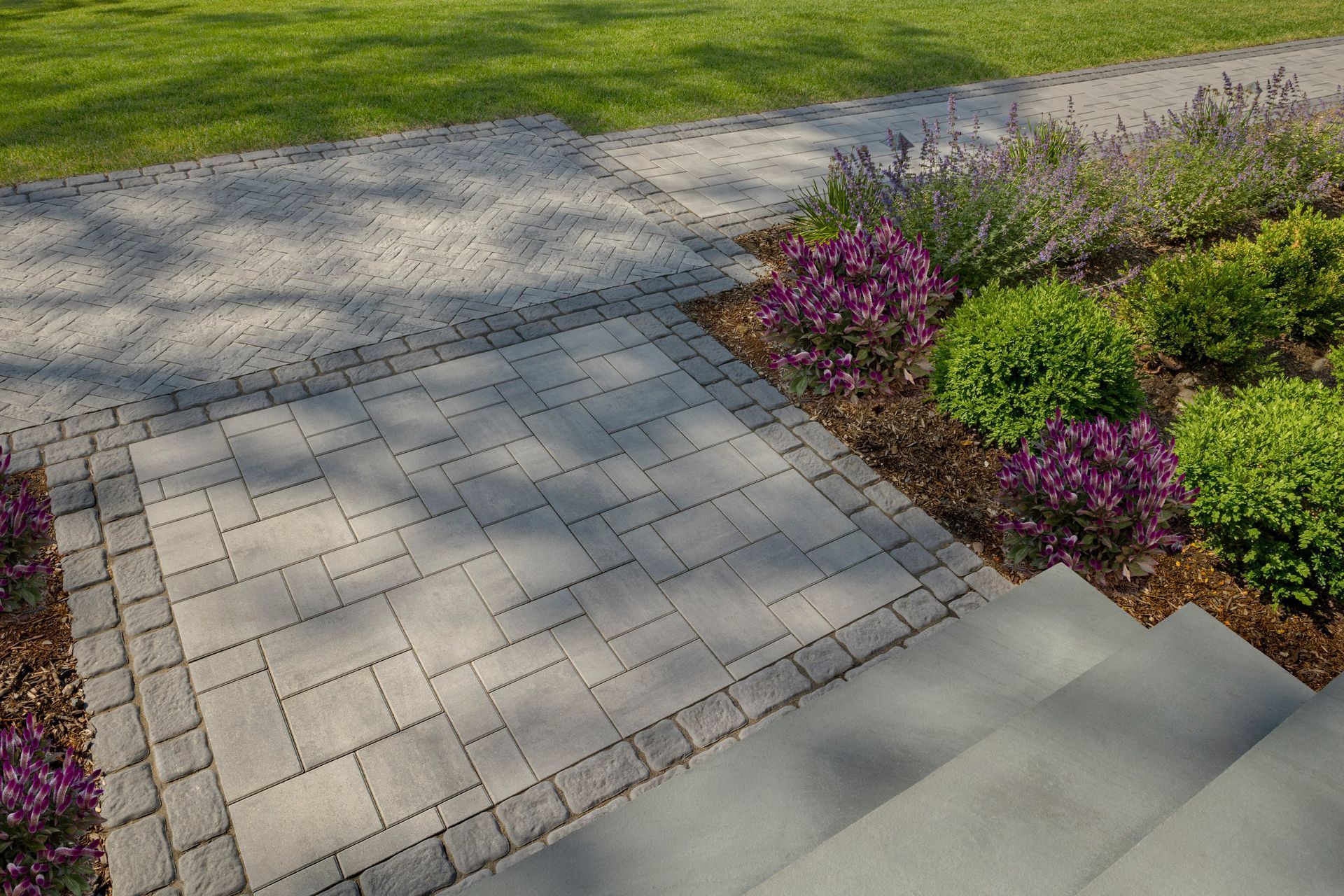 Paved walkway and stone steps beside a landscaped garden with purple flowers and green shrubs