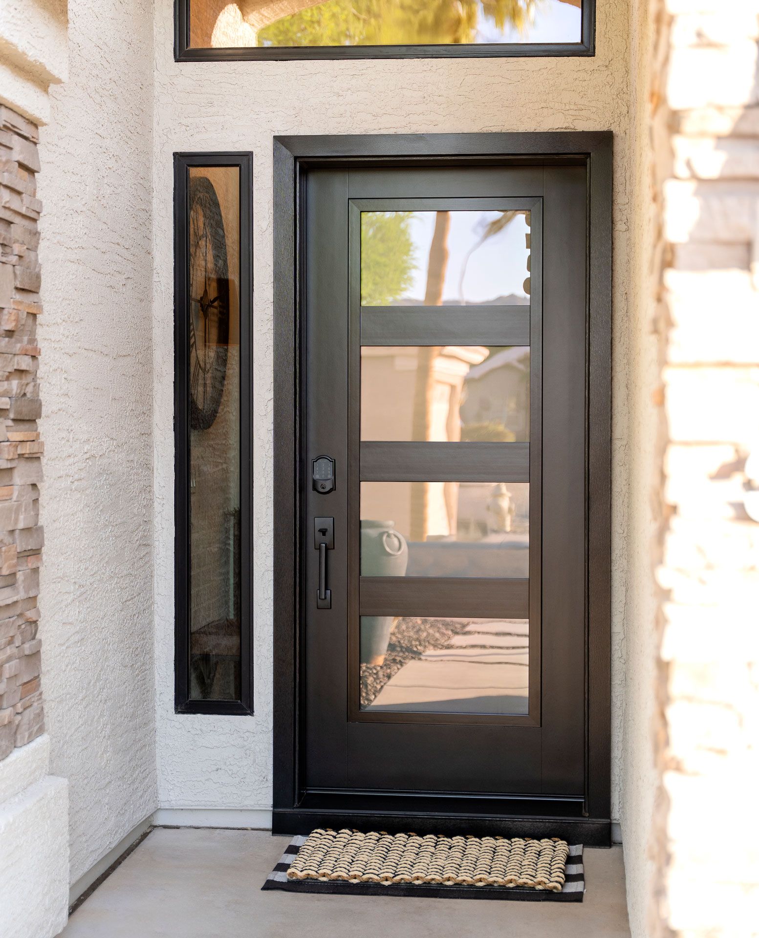 Black front door with sidelights and a welcome mat at a stucco house entry
