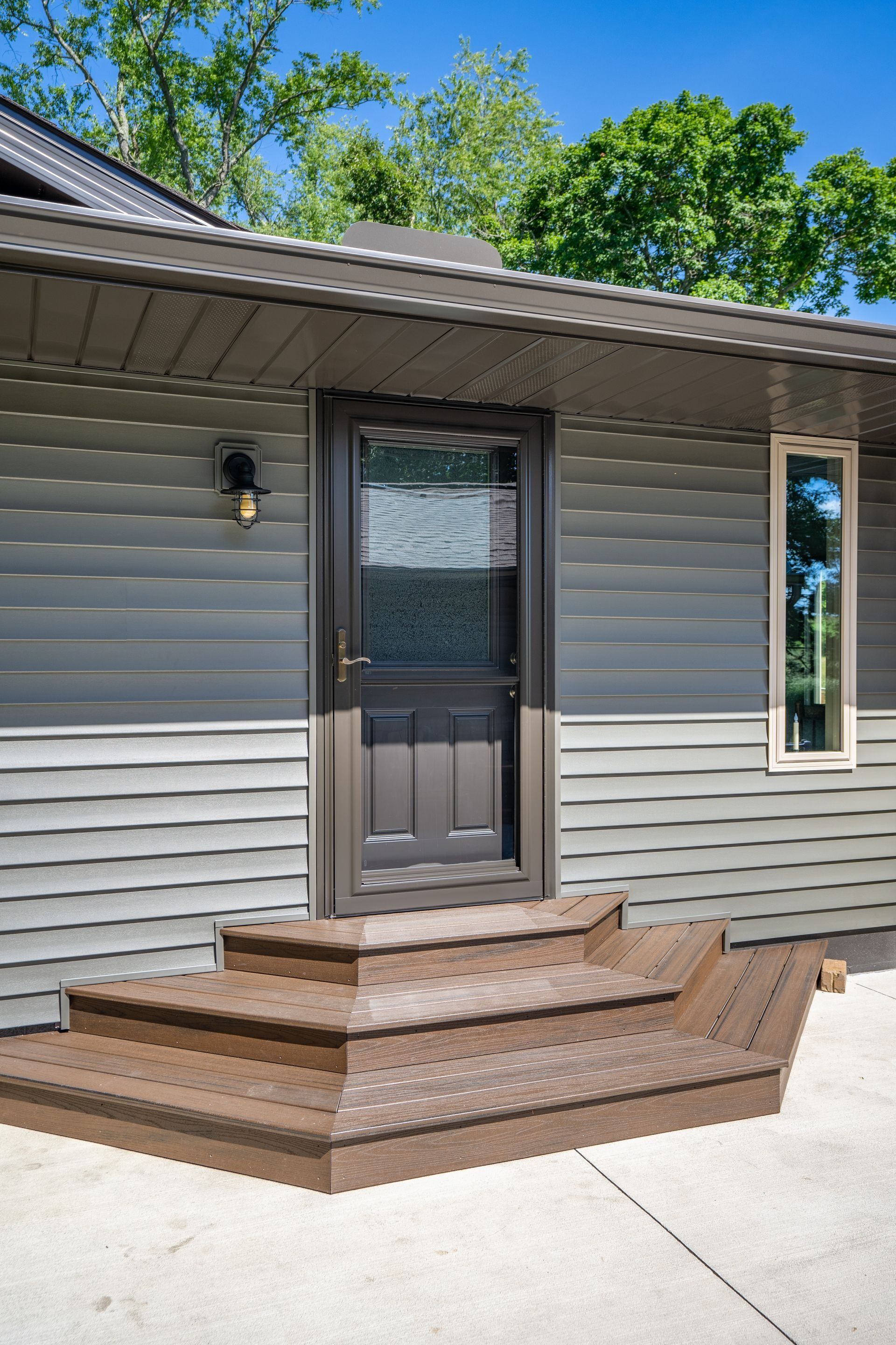 Back door with small brown steps on a gray-sided house under a blue sky