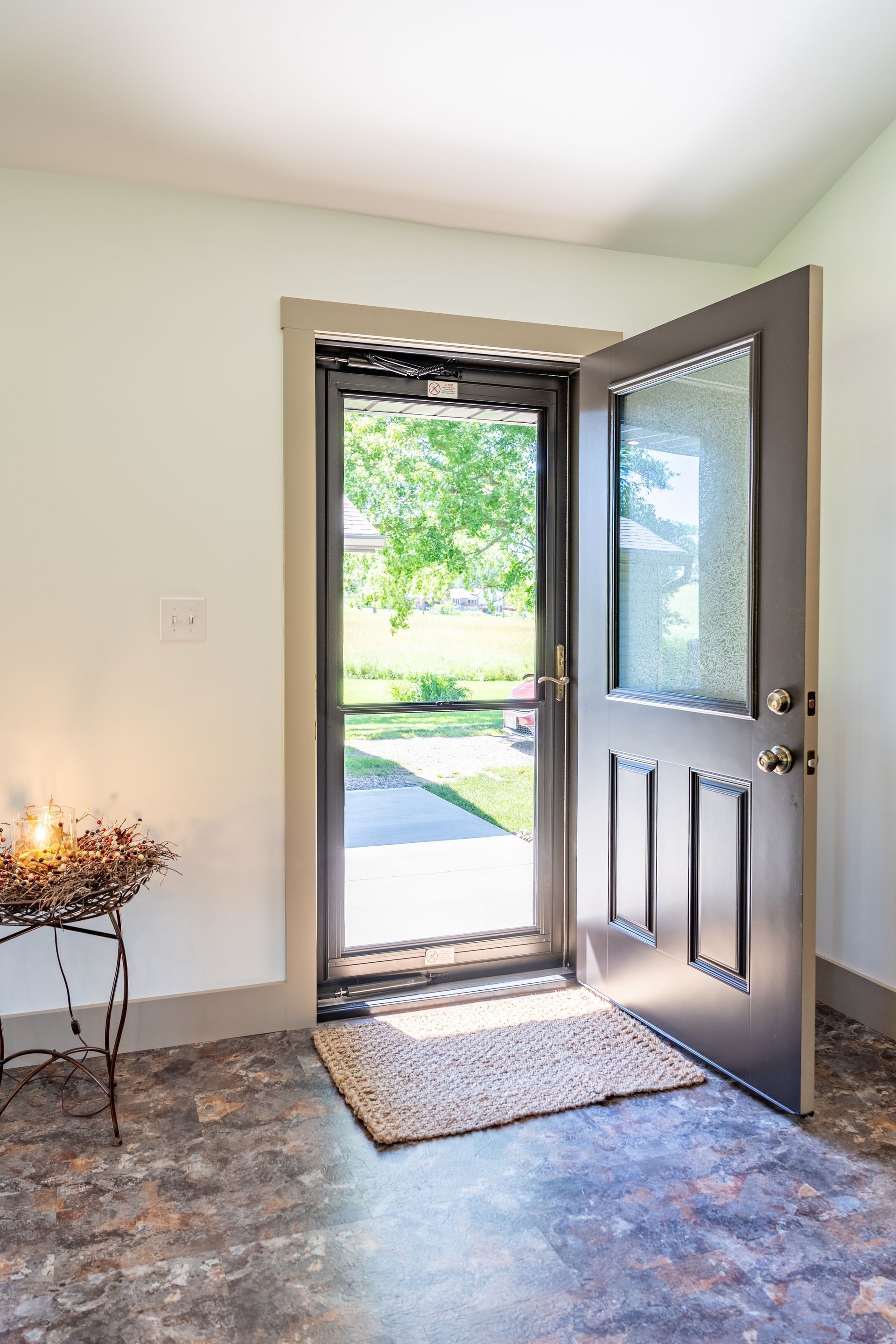 Front door open to a sunny walkway, with a doormat and small decorative plant inside.