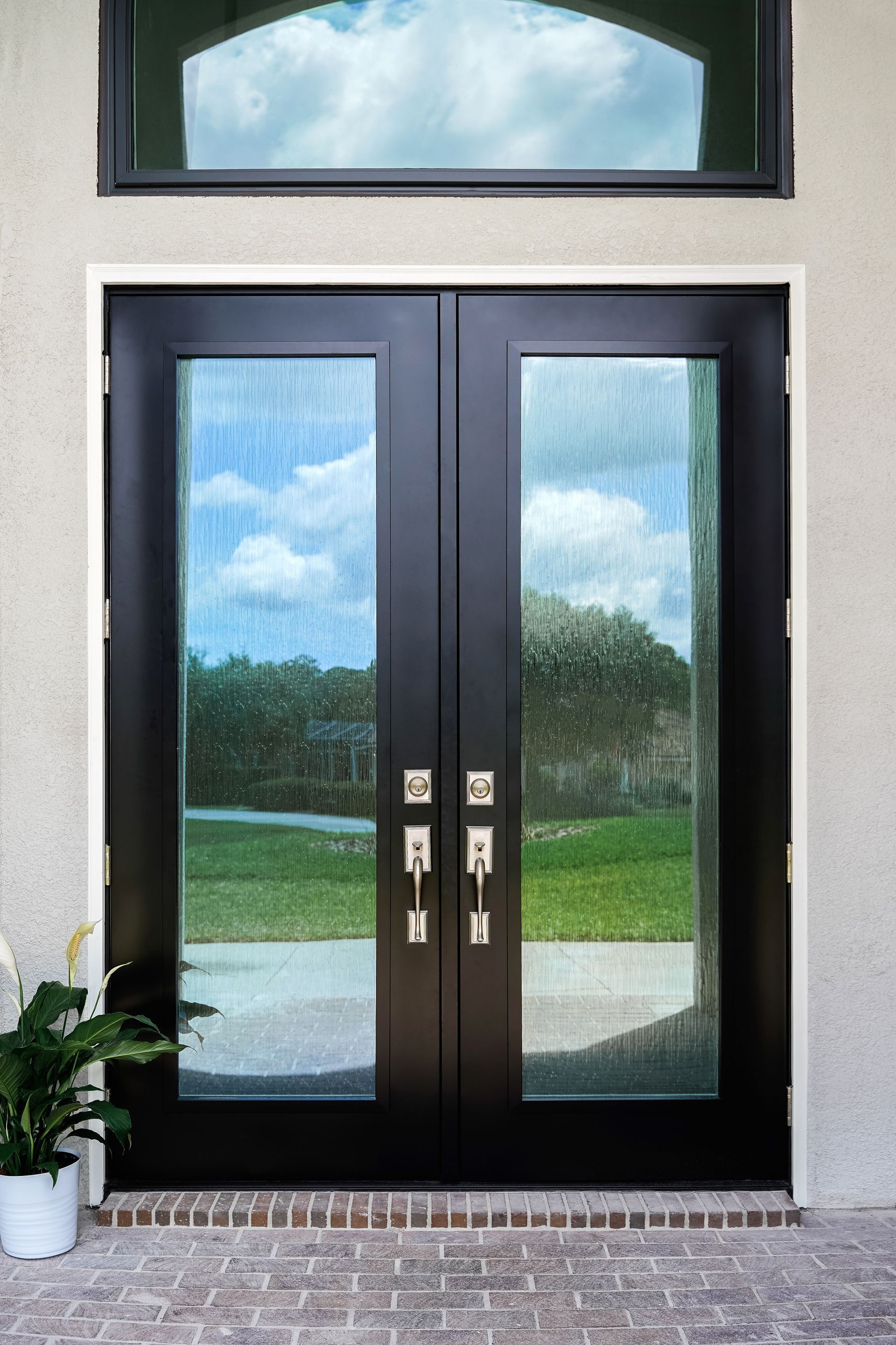 Dark double front doors with glass panels and sidelights, set in a light exterior wall.