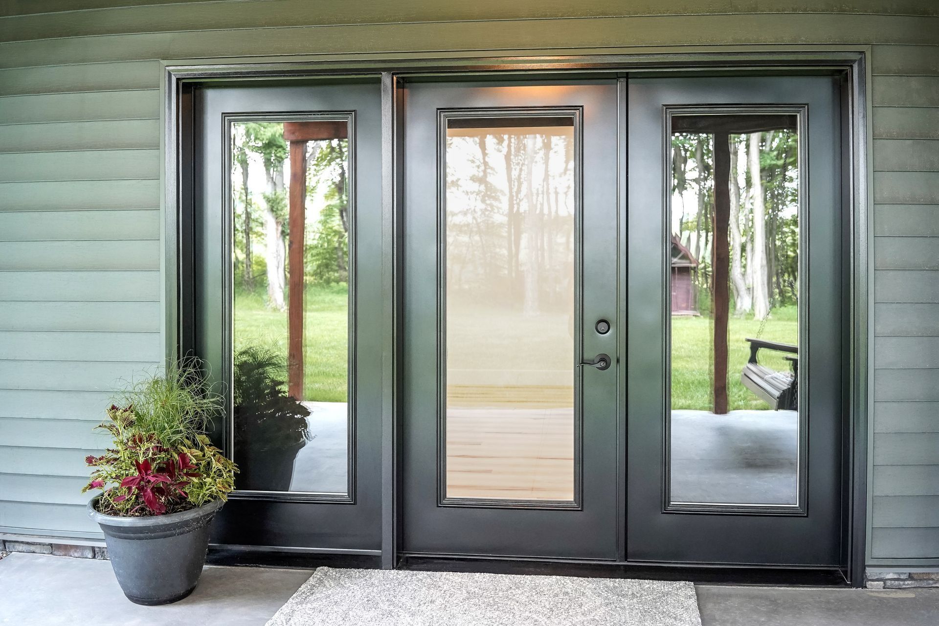 Black-framed glass front door with side panels, next to a potted plant on a porch.