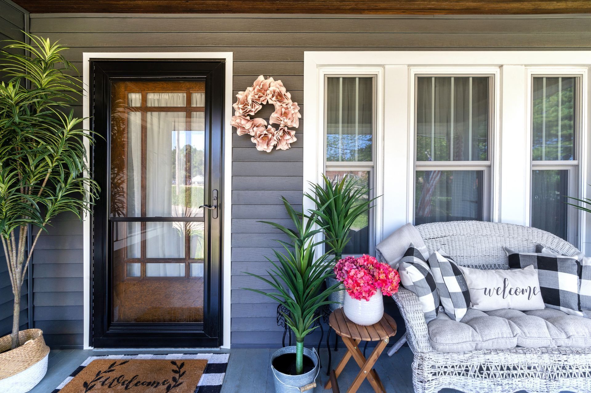 Cozy front porch with black door, white window trim, gray couch, and potted plants