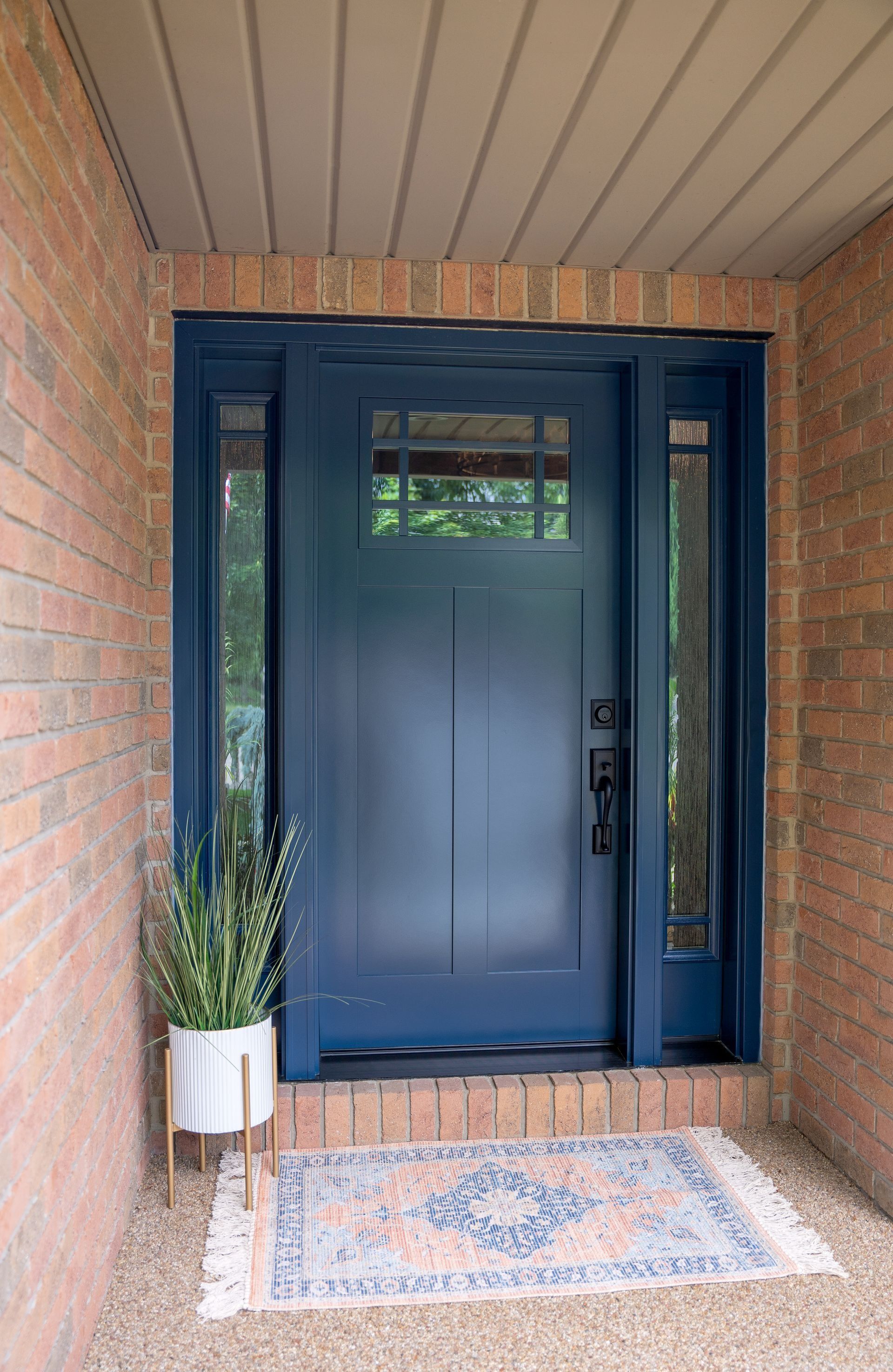 Front porch with navy blue door, brick walls, and a small potted plant beside a patterned doormat.