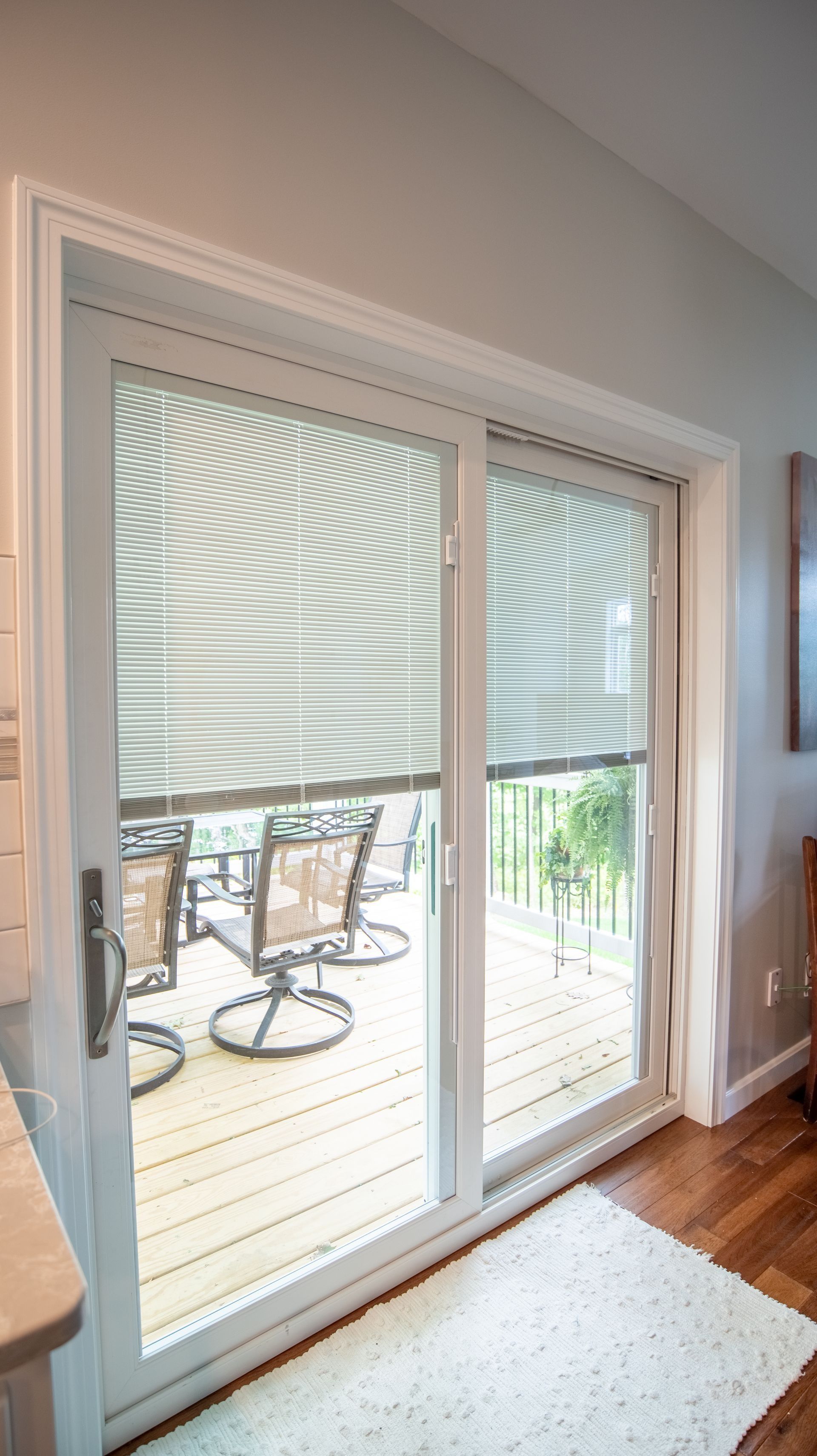 White sliding glass door with blinds opens to a deck with a chair and table.