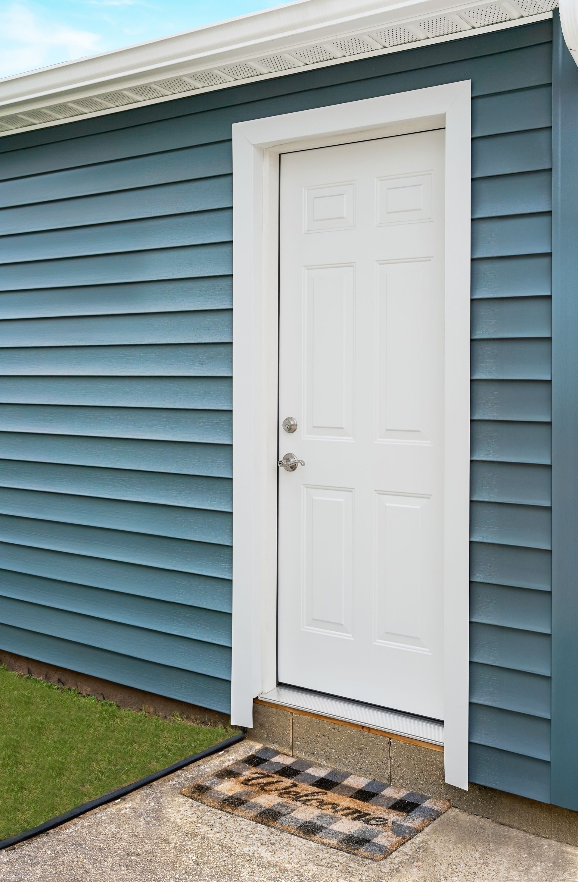 White front door with a small step outside a blue house with horizontal siding