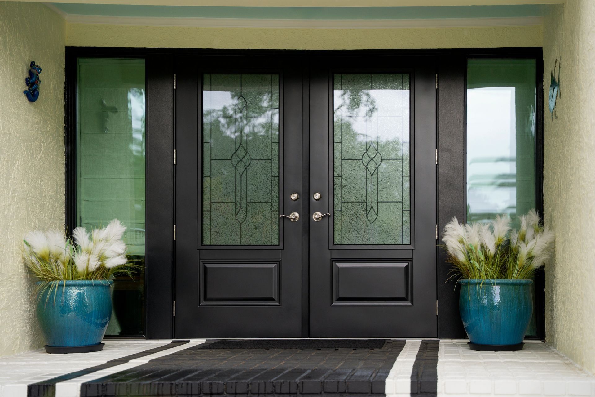 Black double front doors with frosted glass, flanked by blue planters on a porch.