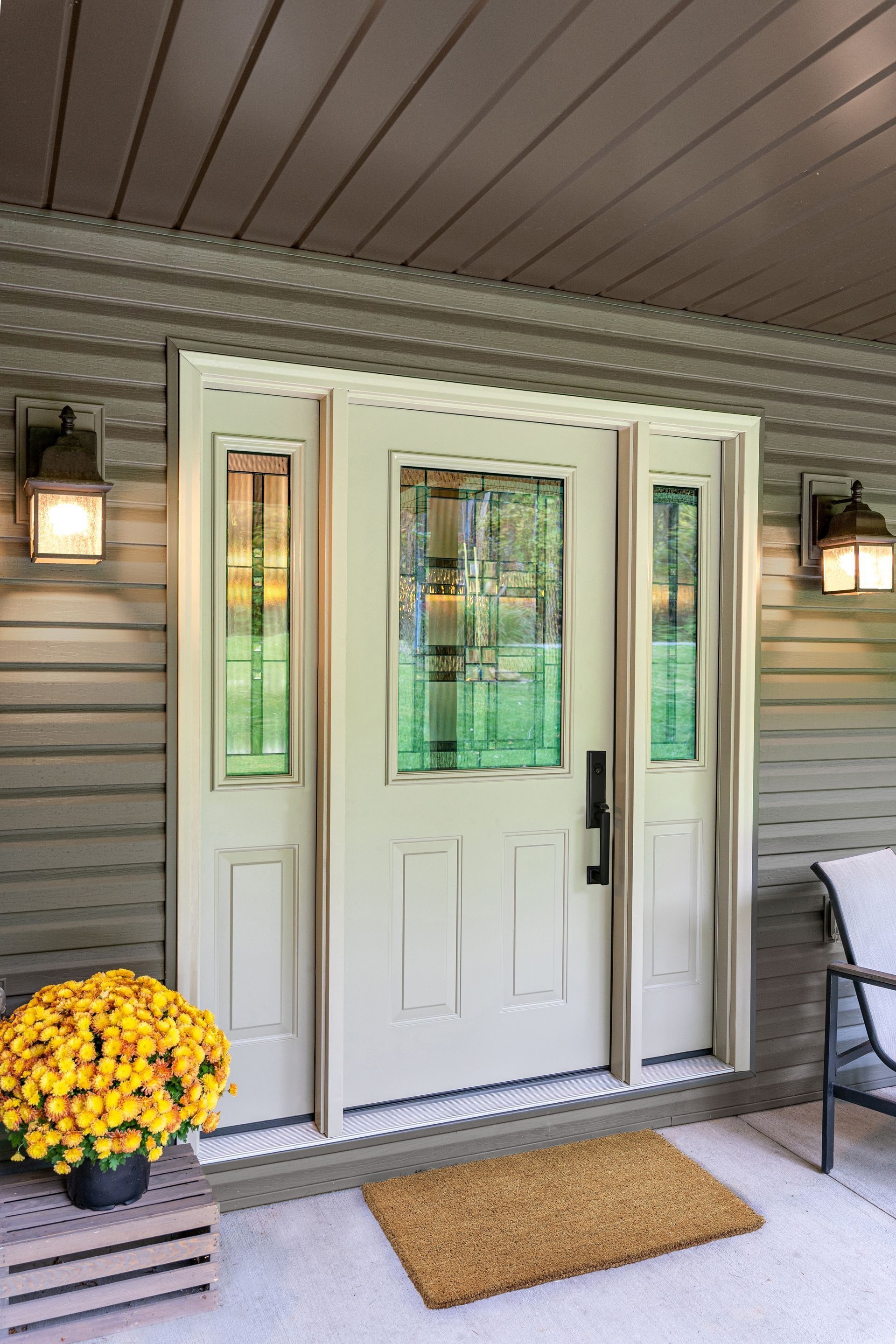 White front door with sidelights, lanterns, and a doormat on a covered porch