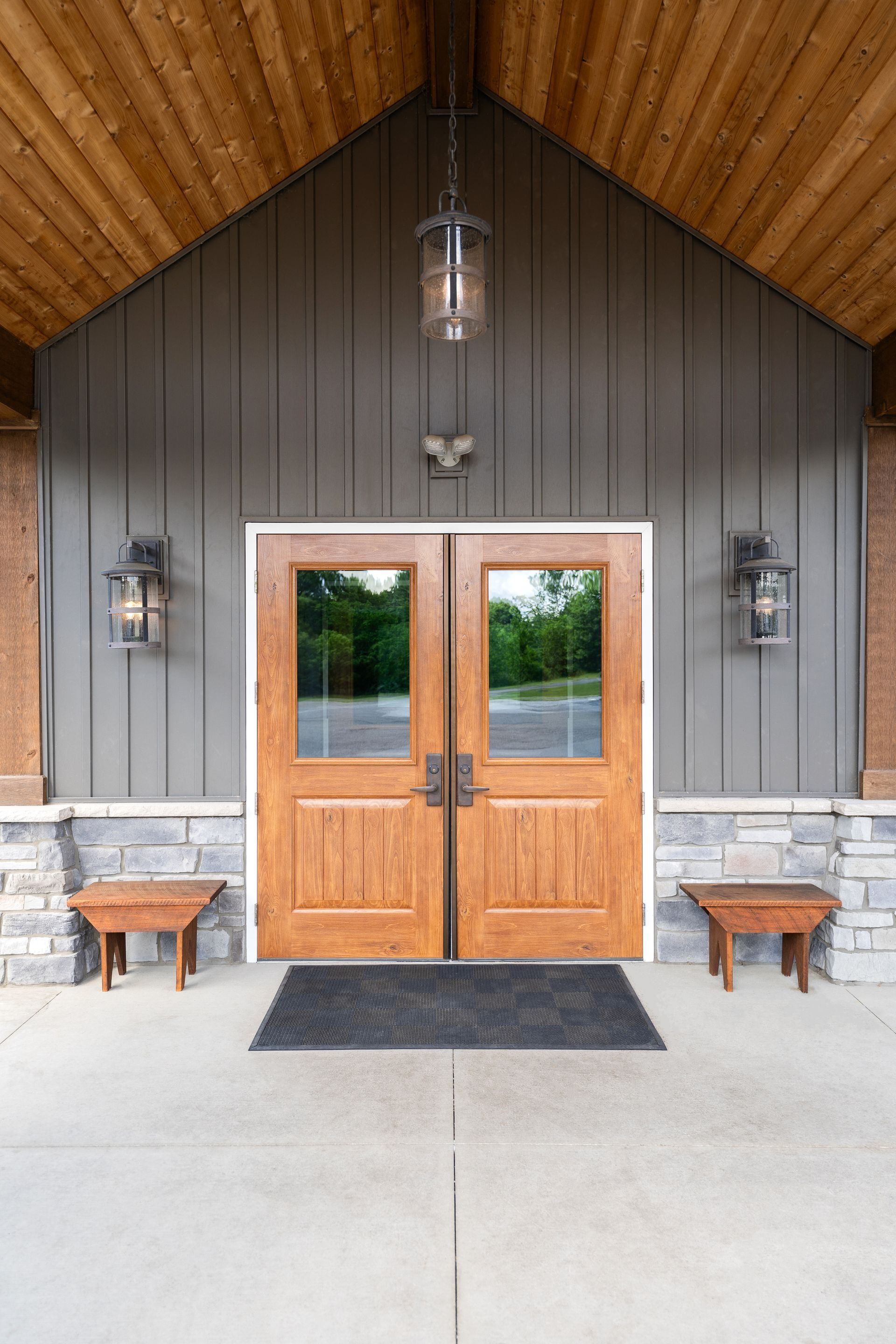 Wooden double front doors with glass panes beneath a covered entryway and lanterns on either side