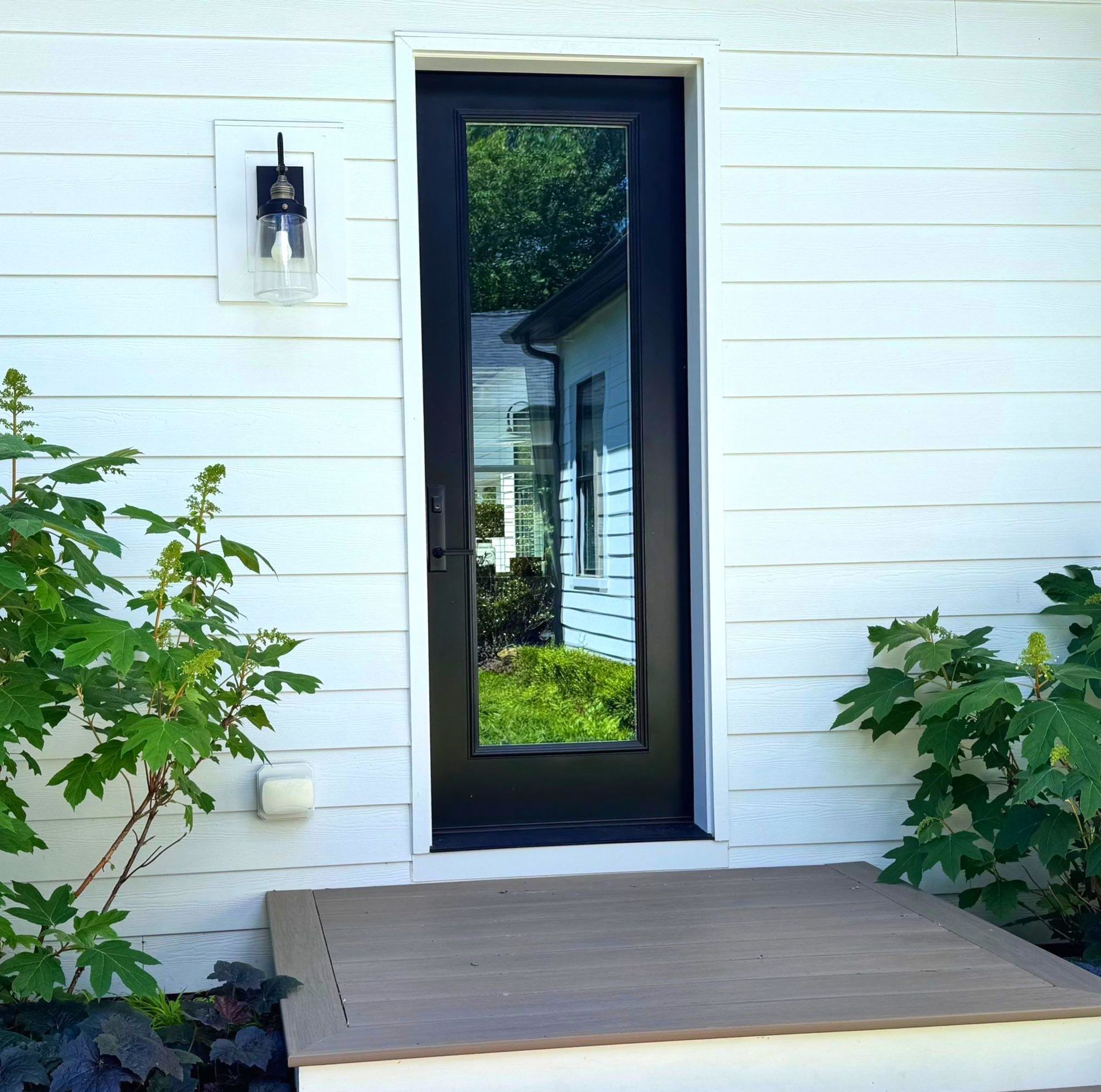 Front entry with a black-framed glass door, white siding, and a small porch.
