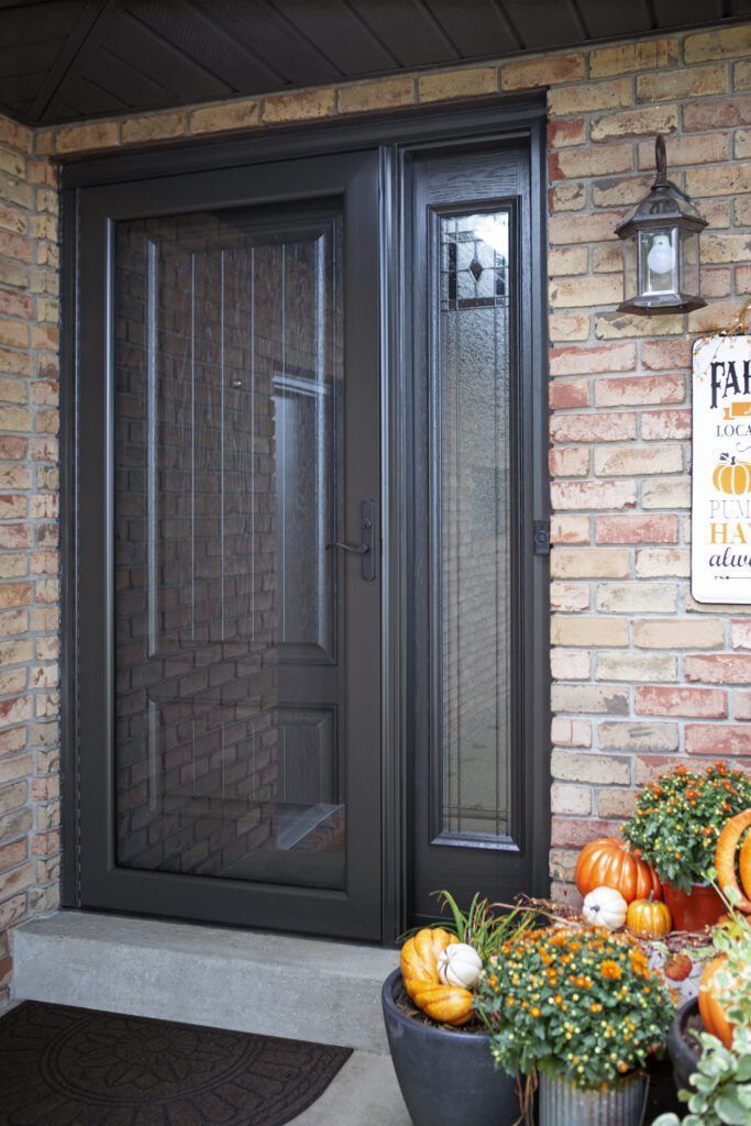 Black front door with sidelights on a brick house, decorated with pumpkins and fall flowers by the entry