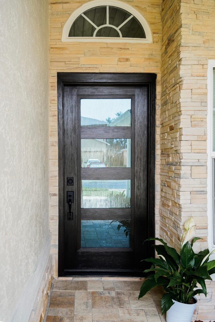 Front door with black frame, glass panels, and an arched window above, set in a stone entryway