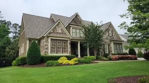 Large suburban house with a steep roof, stone facade, manicured lawn, and landscaped shrubs