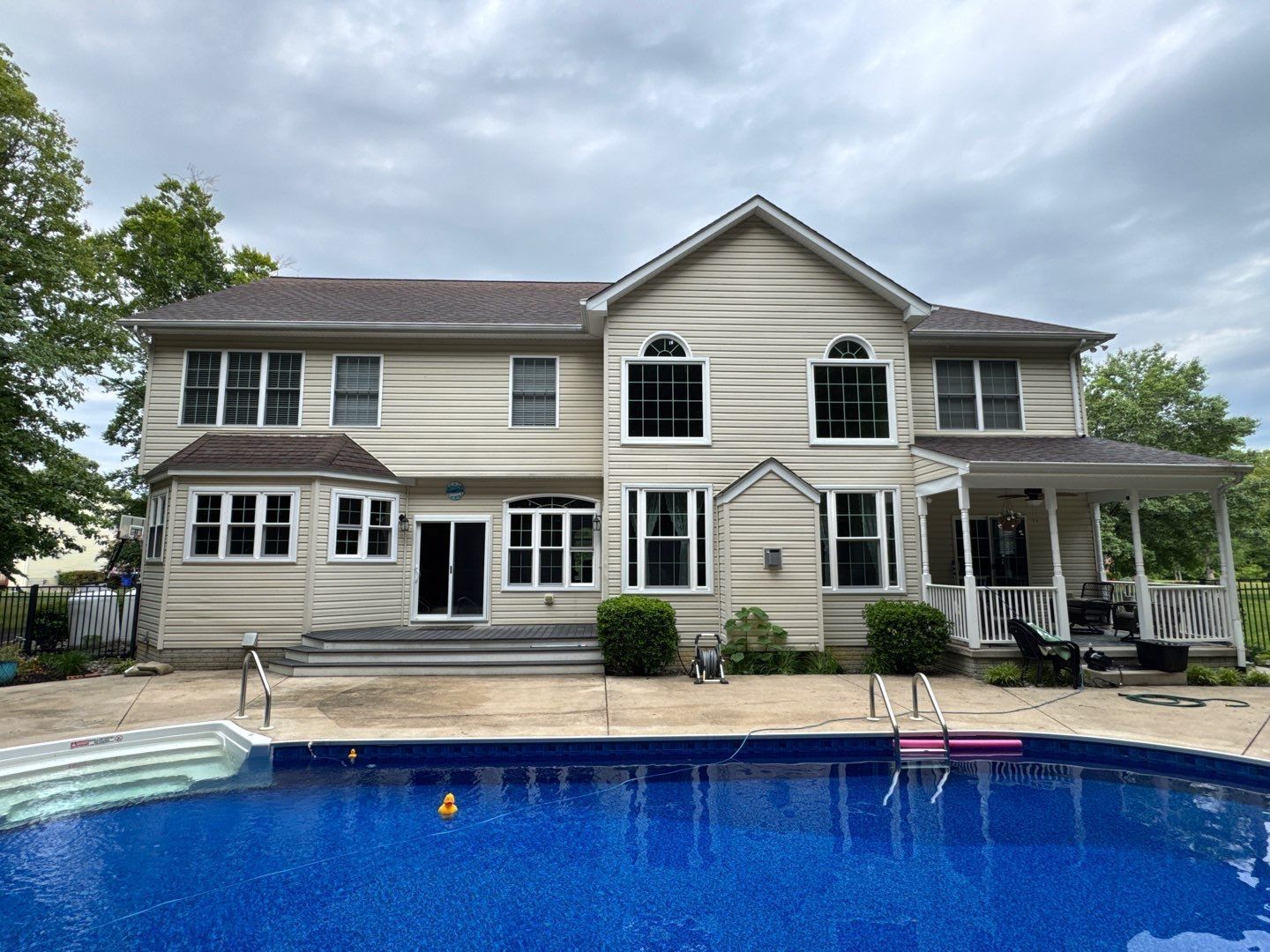 Two-story house with a backyard swimming pool under a cloudy sky.
