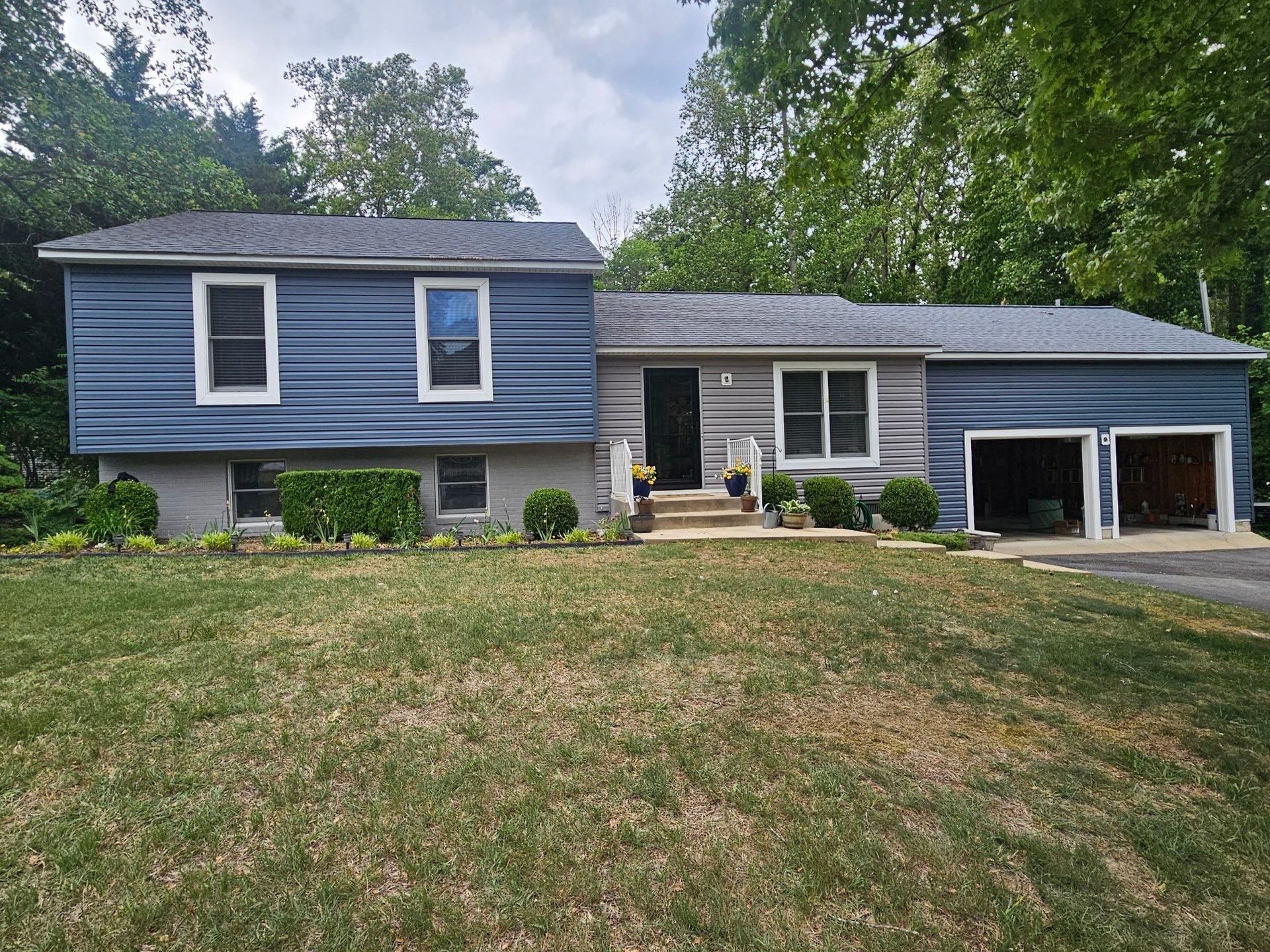 Blue split-level house with attached two-car garage and large front lawn under a partly cloudy sky.