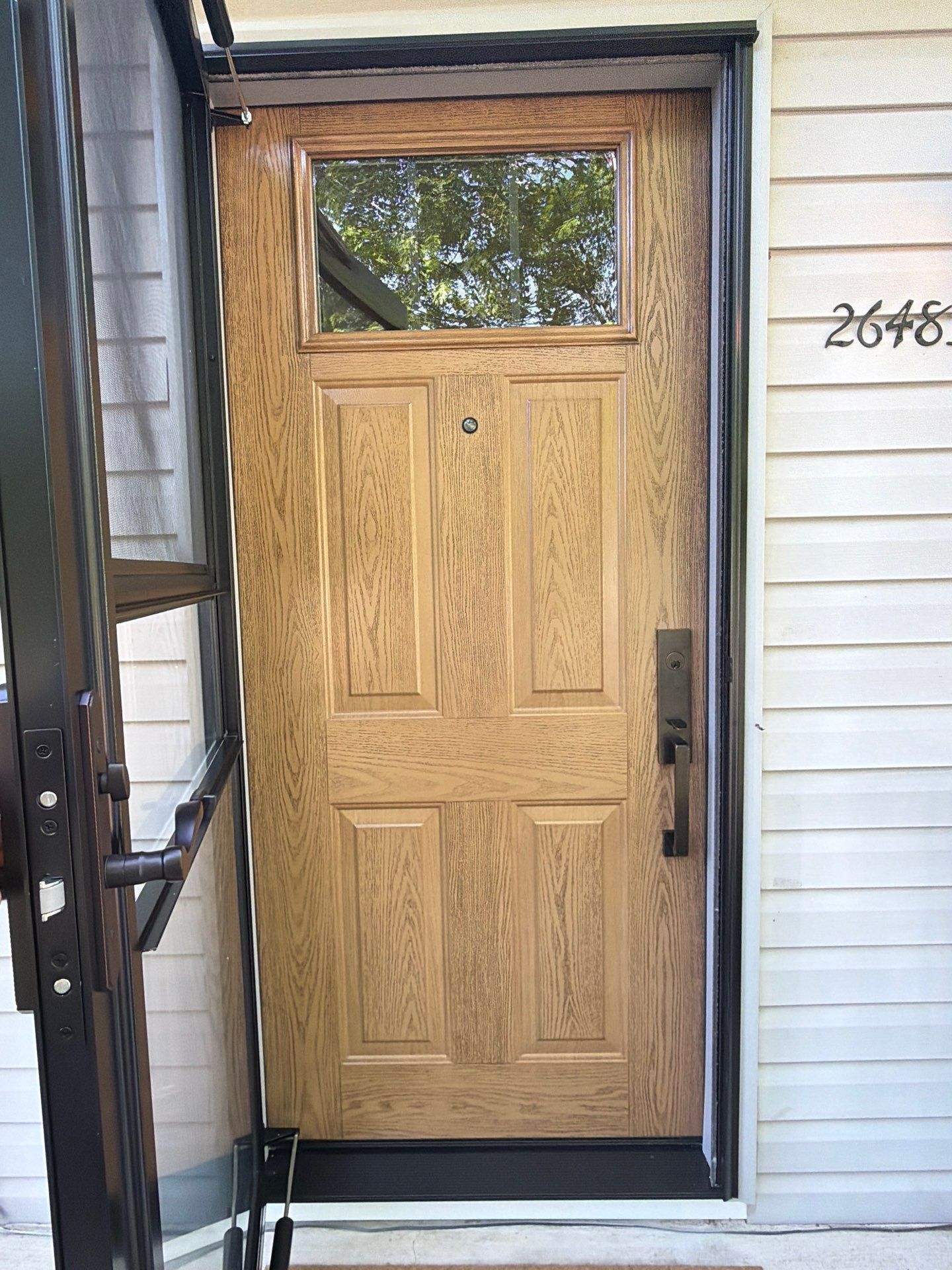 Front entry with a light wood door, black screen door, and house number on white siding.