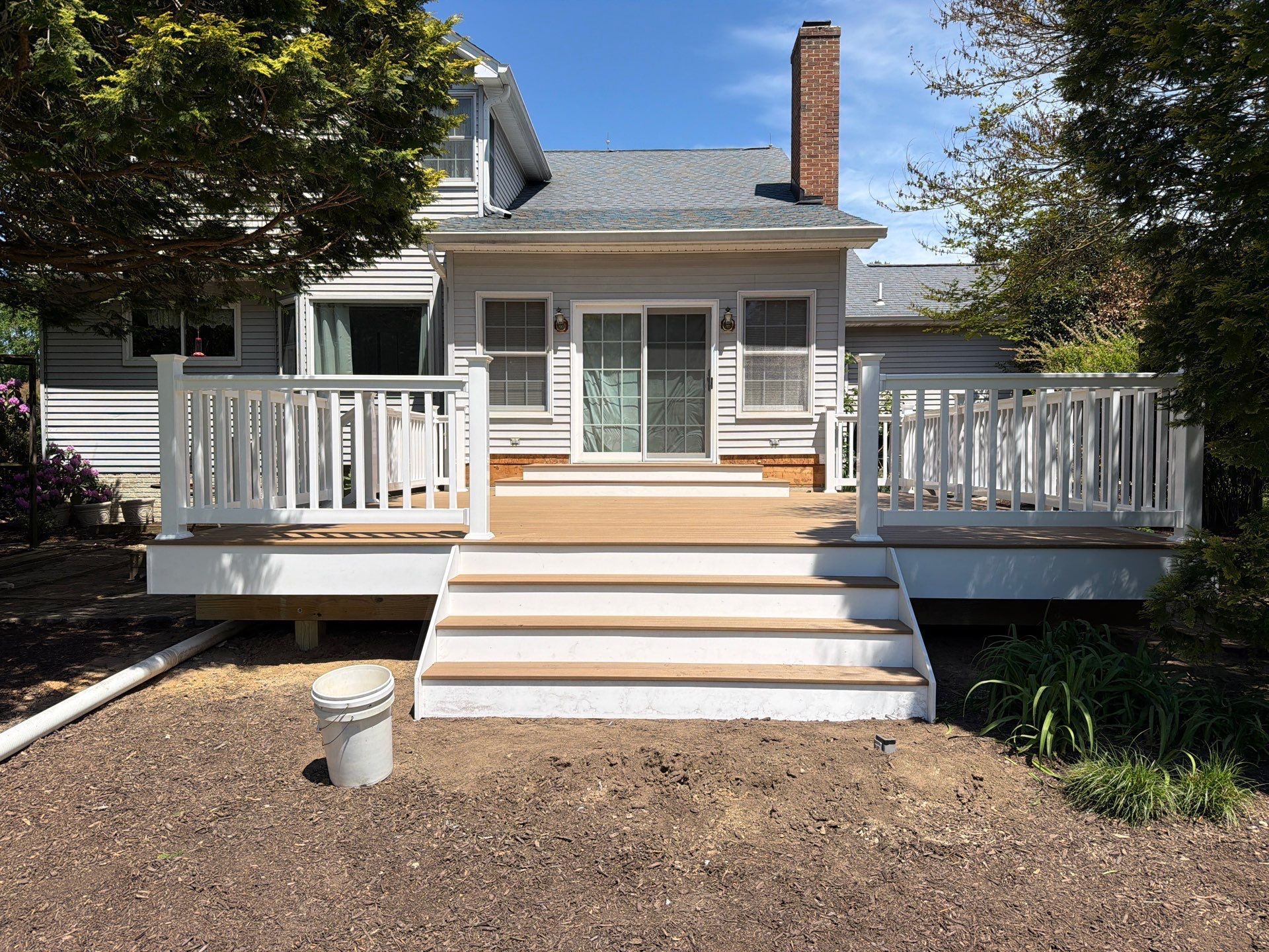 White house front porch with steps, railings, and a brick chimney behind a dirt yard.