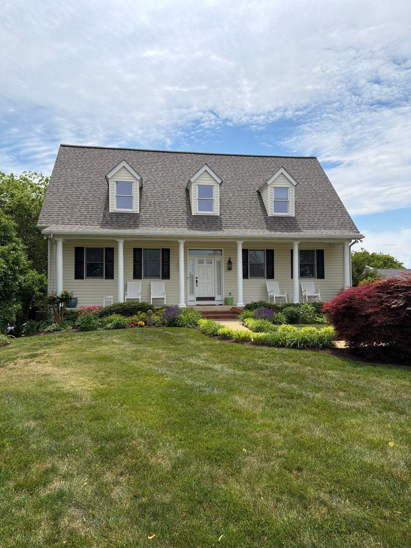 Suburban house with gray roof, white siding, and a front lawn under a cloudy sky.