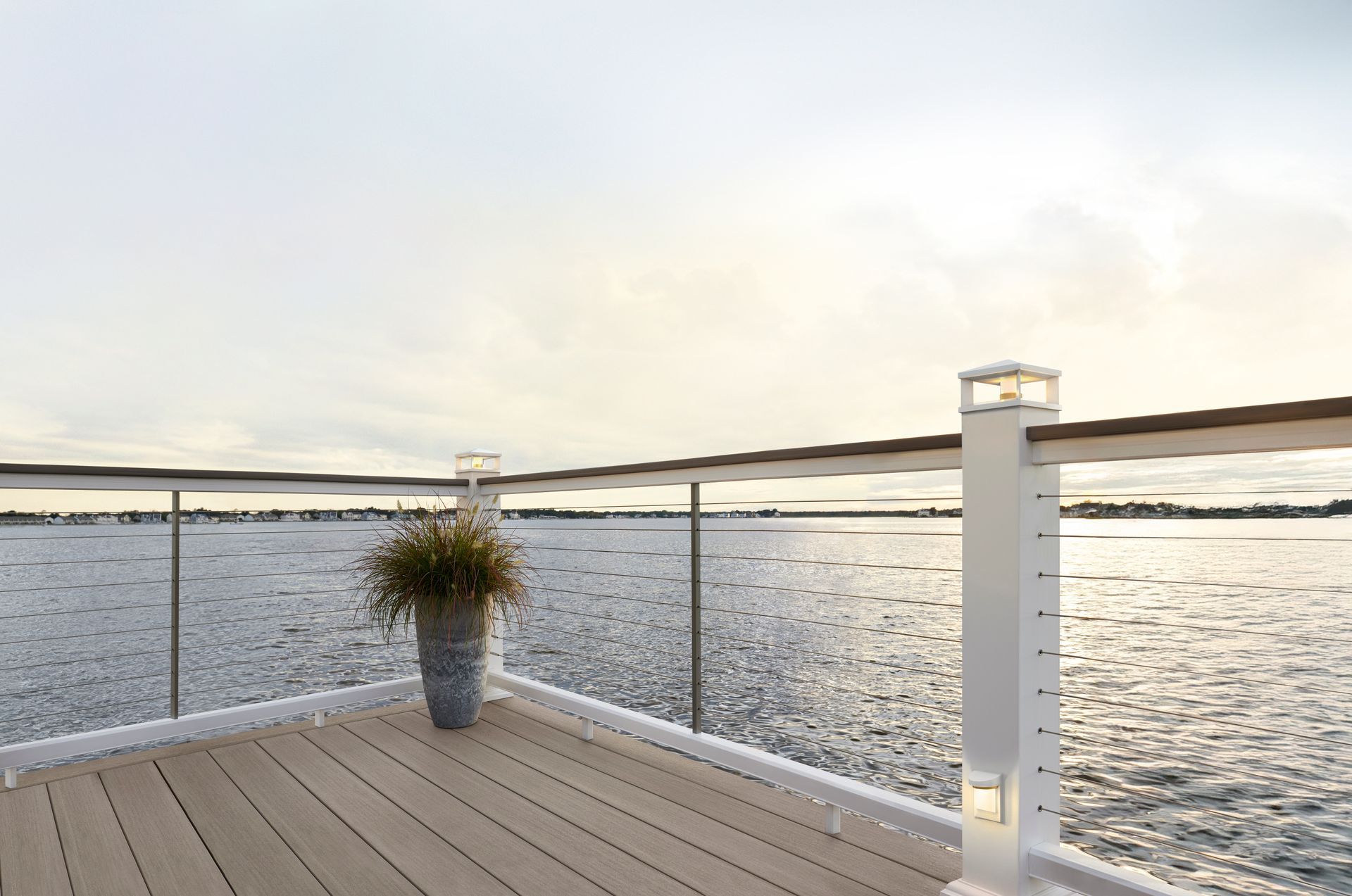 Deck overlooking calm water at sunset, with glass railing and potted plant