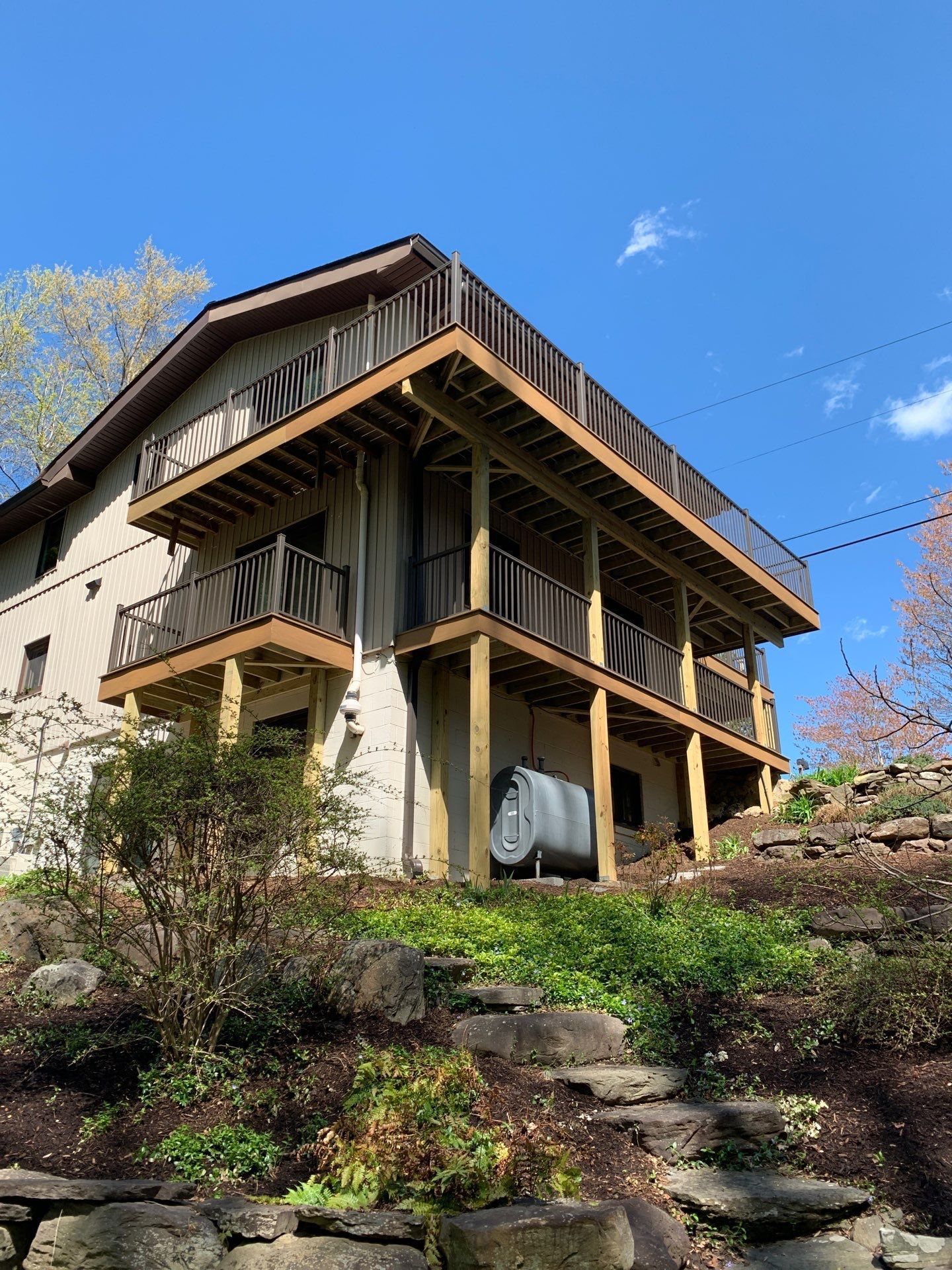 Wooden house on a hillside with stone steps, surrounded by greenery under a blue sky