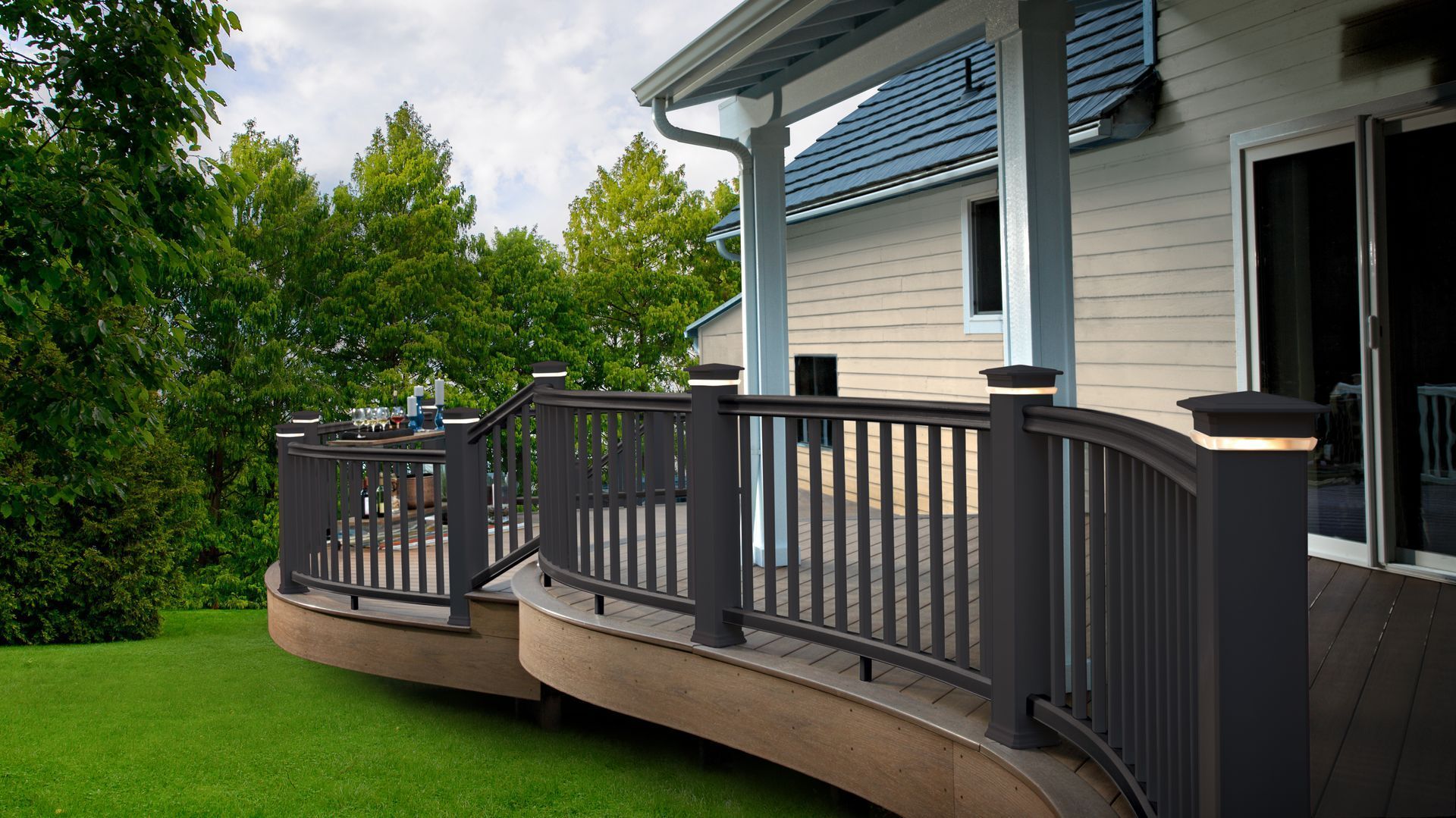 Curved wooden deck attached to a house, overlooking a green lawn and trees.