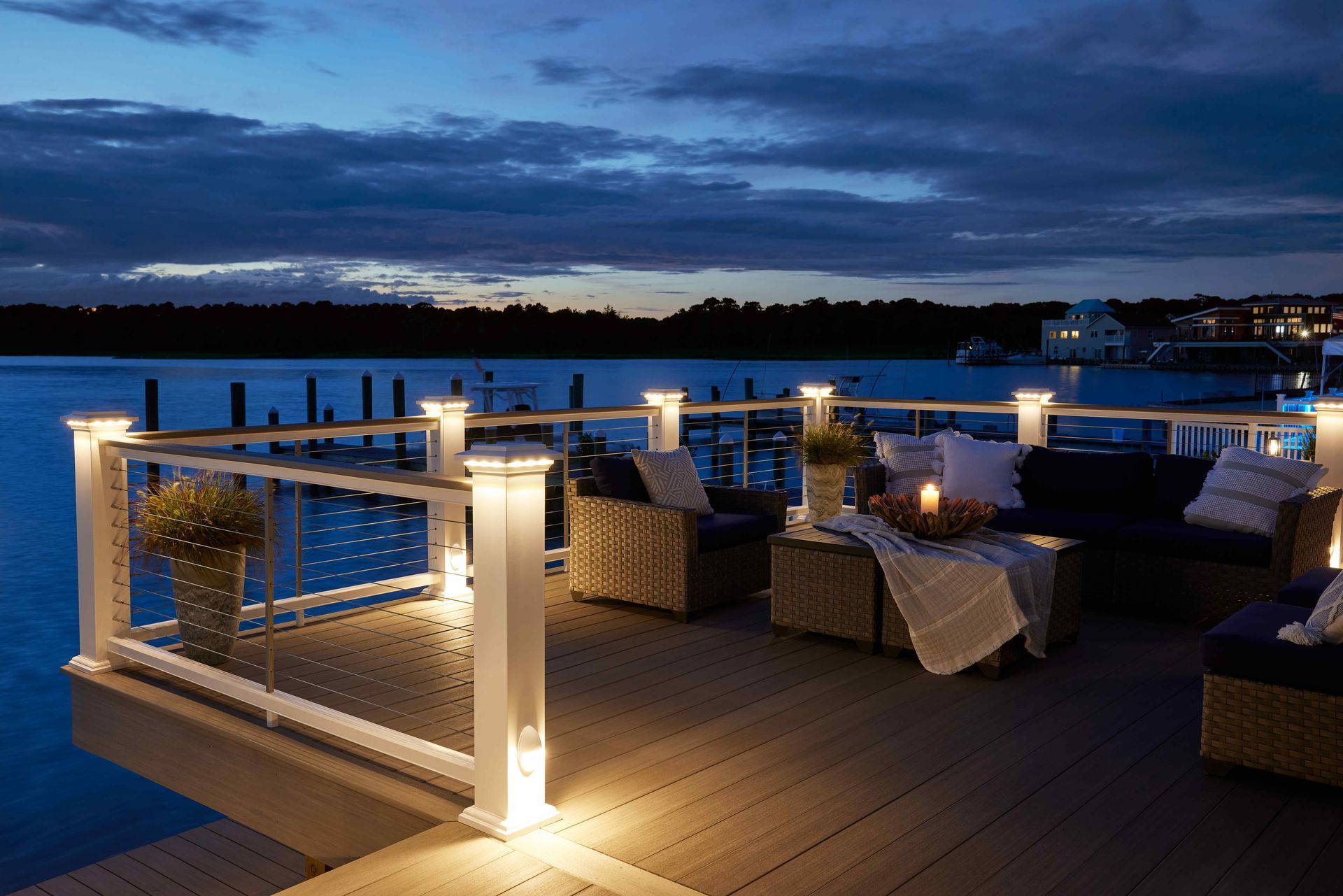 Rooftop deck with lit lounge seating overlooking water at dusk