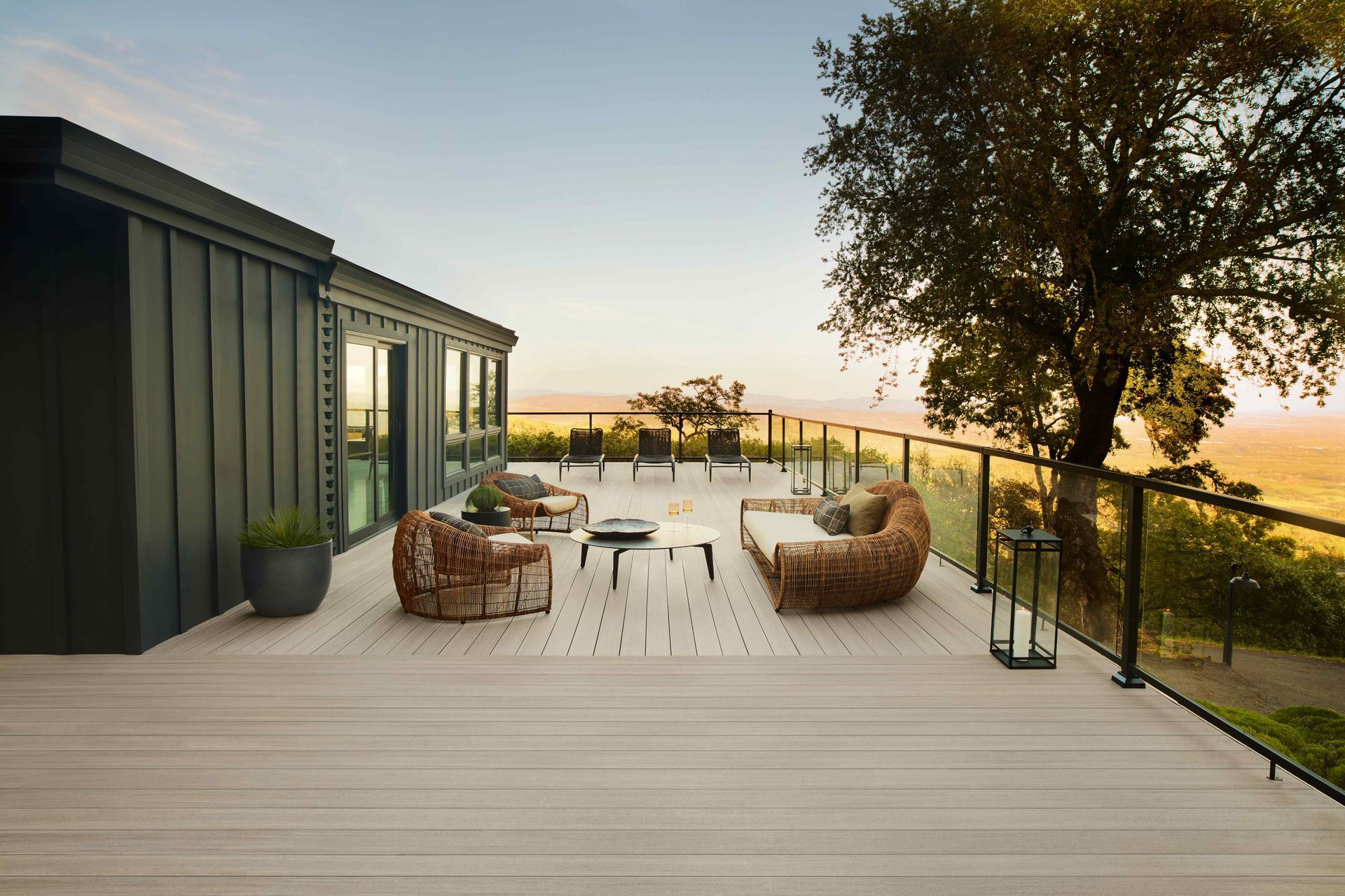 Modern deck with wicker chairs, small table, and sunset view beside a dark-sided house