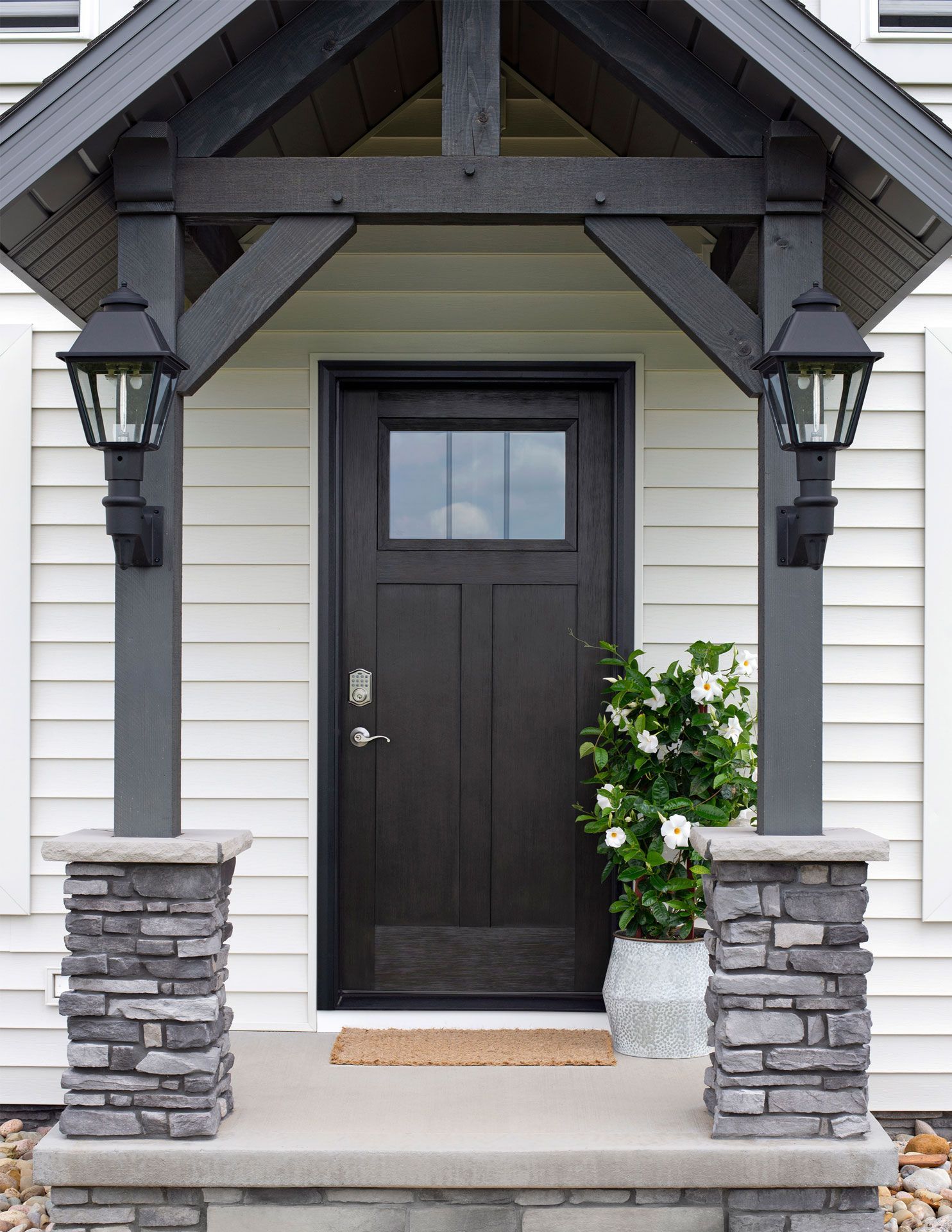 Front entrance with dark door, stone columns, hanging lanterns, and potted flowers