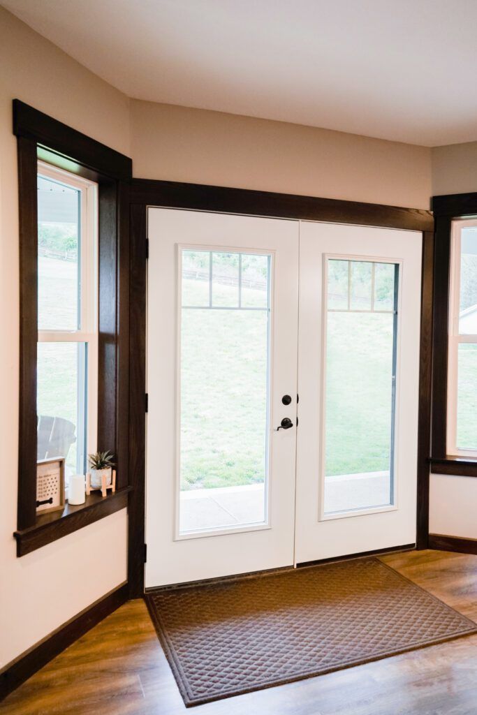 Entryway with white French doors, dark wood trim, sidelights, and a woven doormat on hardwood floor
