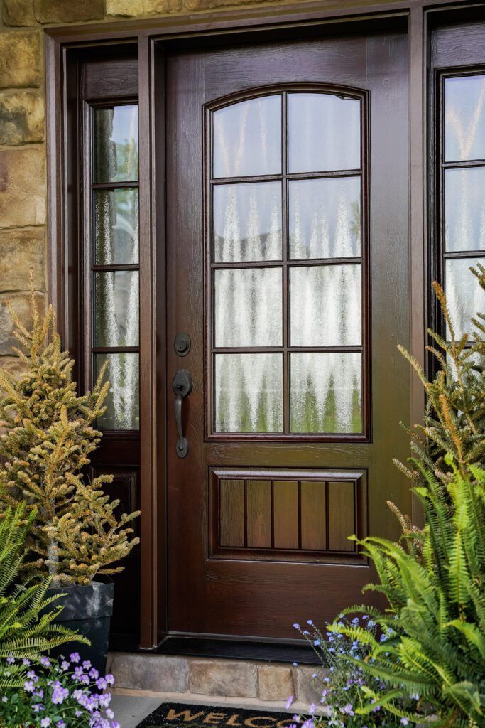 Dark wooden front door with glass panels, framed by stone and potted greenery
