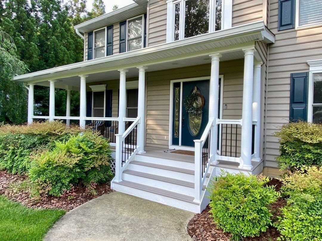 Front porch of a beige house with white columns, steps, and trimmed shrubs along the entryway.