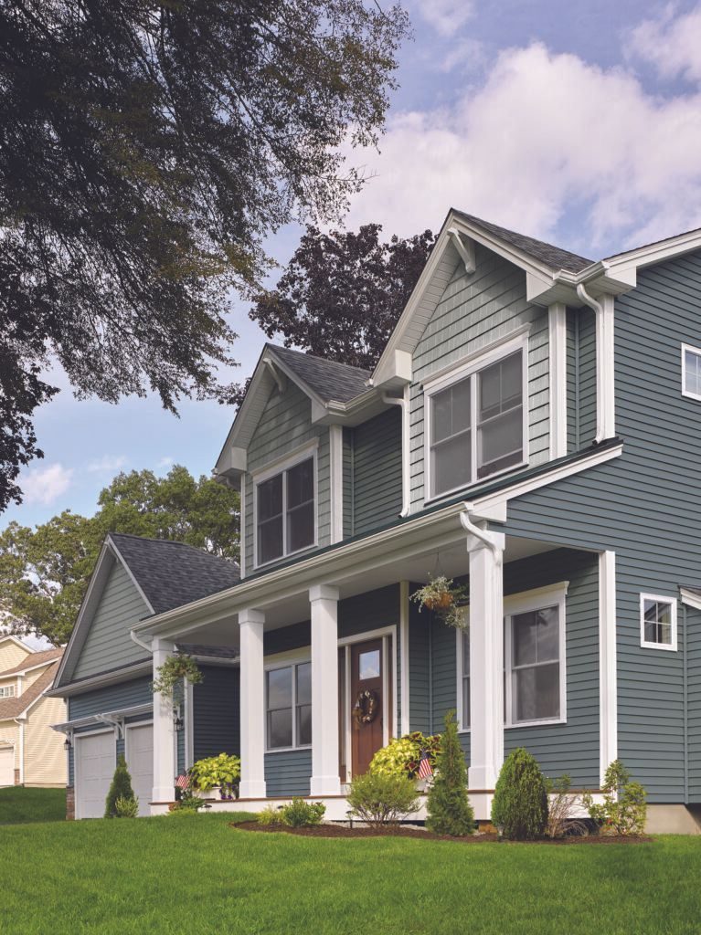 Blue-gray two-story suburban house with white trim, front porch, and manicured lawn