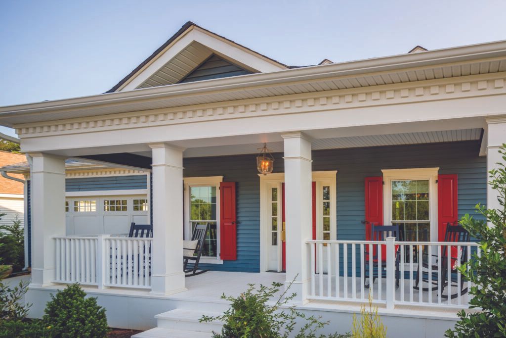 Front porch of a white house with red shutters and a white railing, seen in daylight.