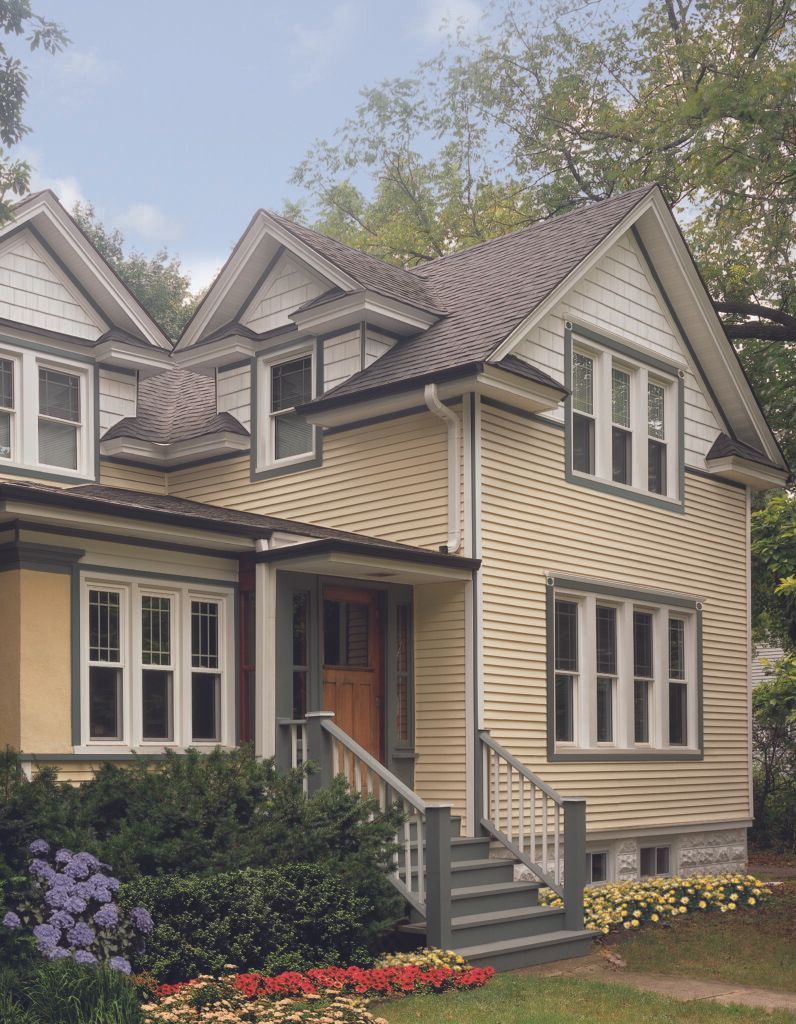 Yellow house with gray trim, front steps, and flower beds amid trees