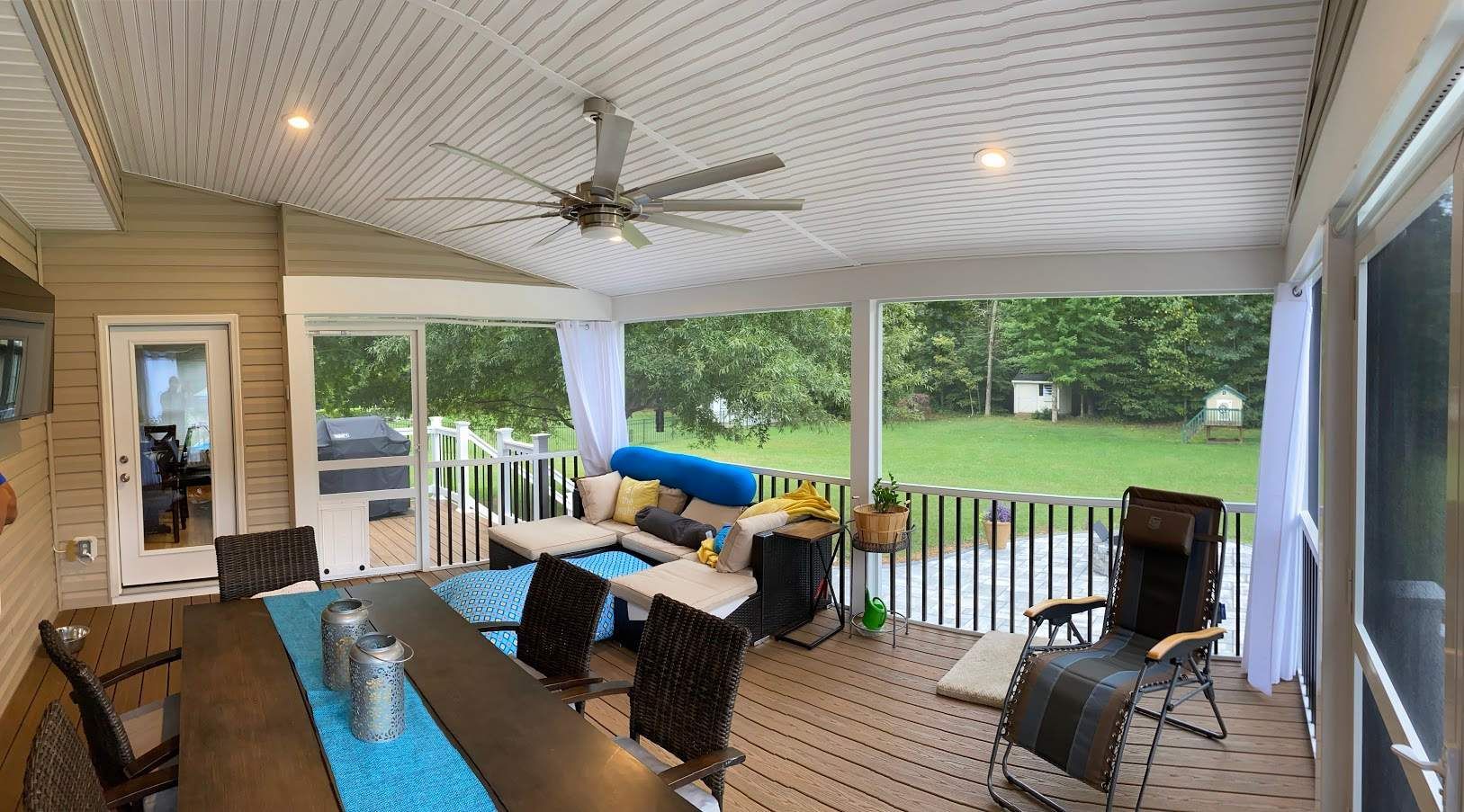 Covered patio with dining table, chairs, ceiling fan, grill, and view of a green backyard.