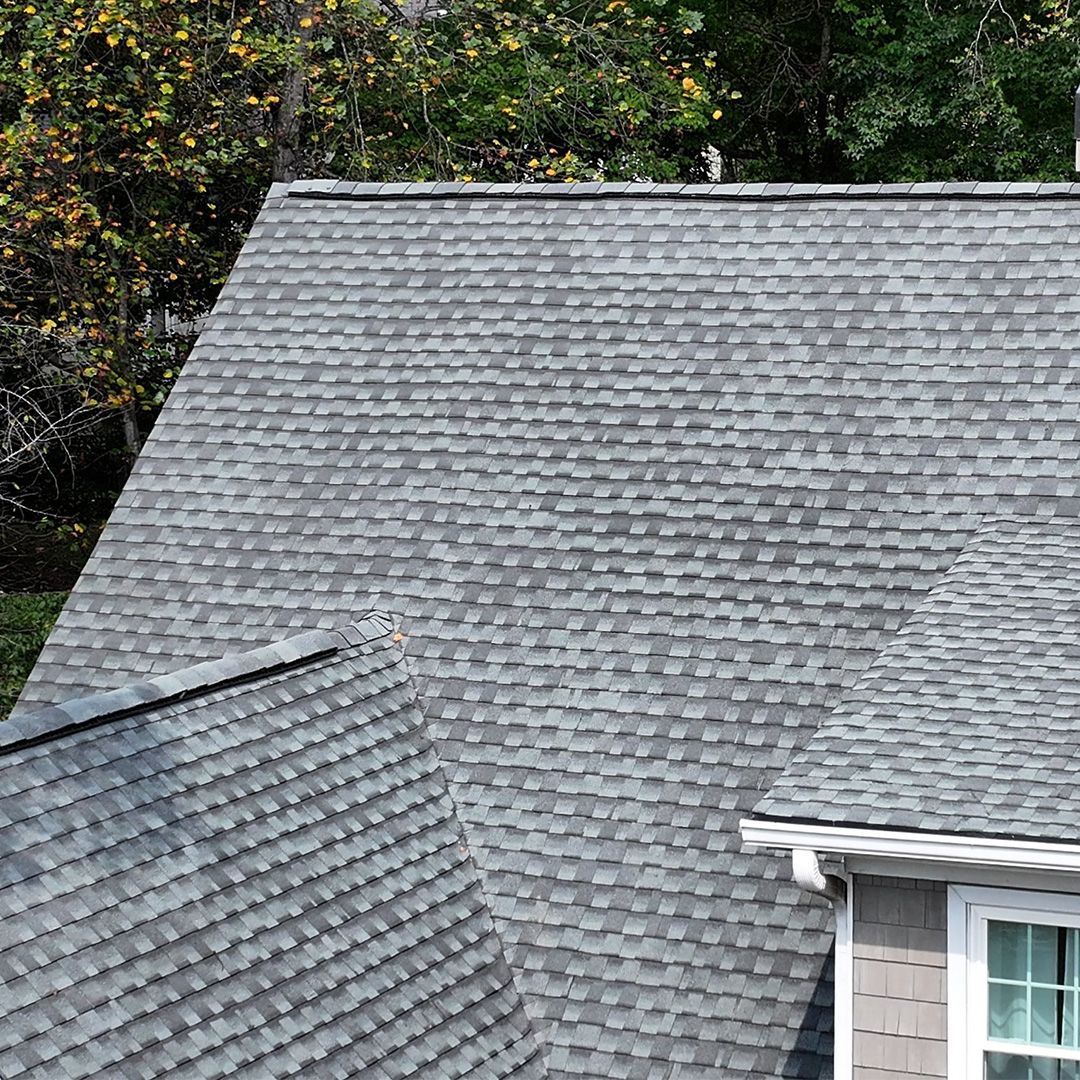 Gray shingled roof with a dormer and visible window under trees