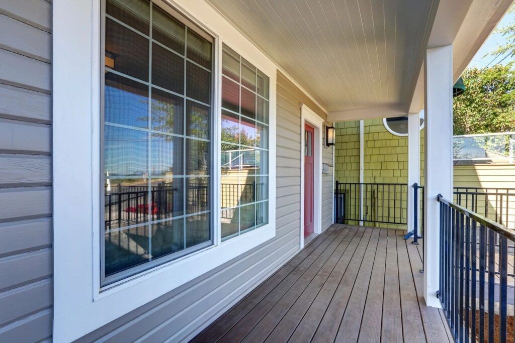Front porch with white siding, large windows, red door, and black railing overlooking a street.