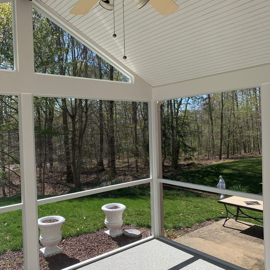 Covered screened porch with white ceiling, potted plants, and a wooded backyard view.