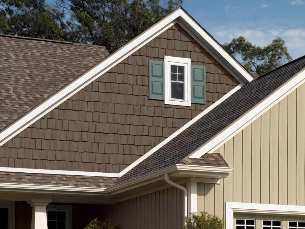 House exterior with brown shingle siding, white trim, and a dormer window with green shutters