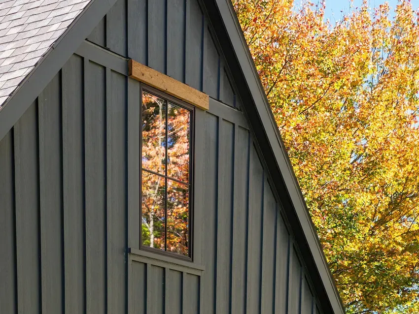 Gray house gable with narrow window and autumn tree reflections