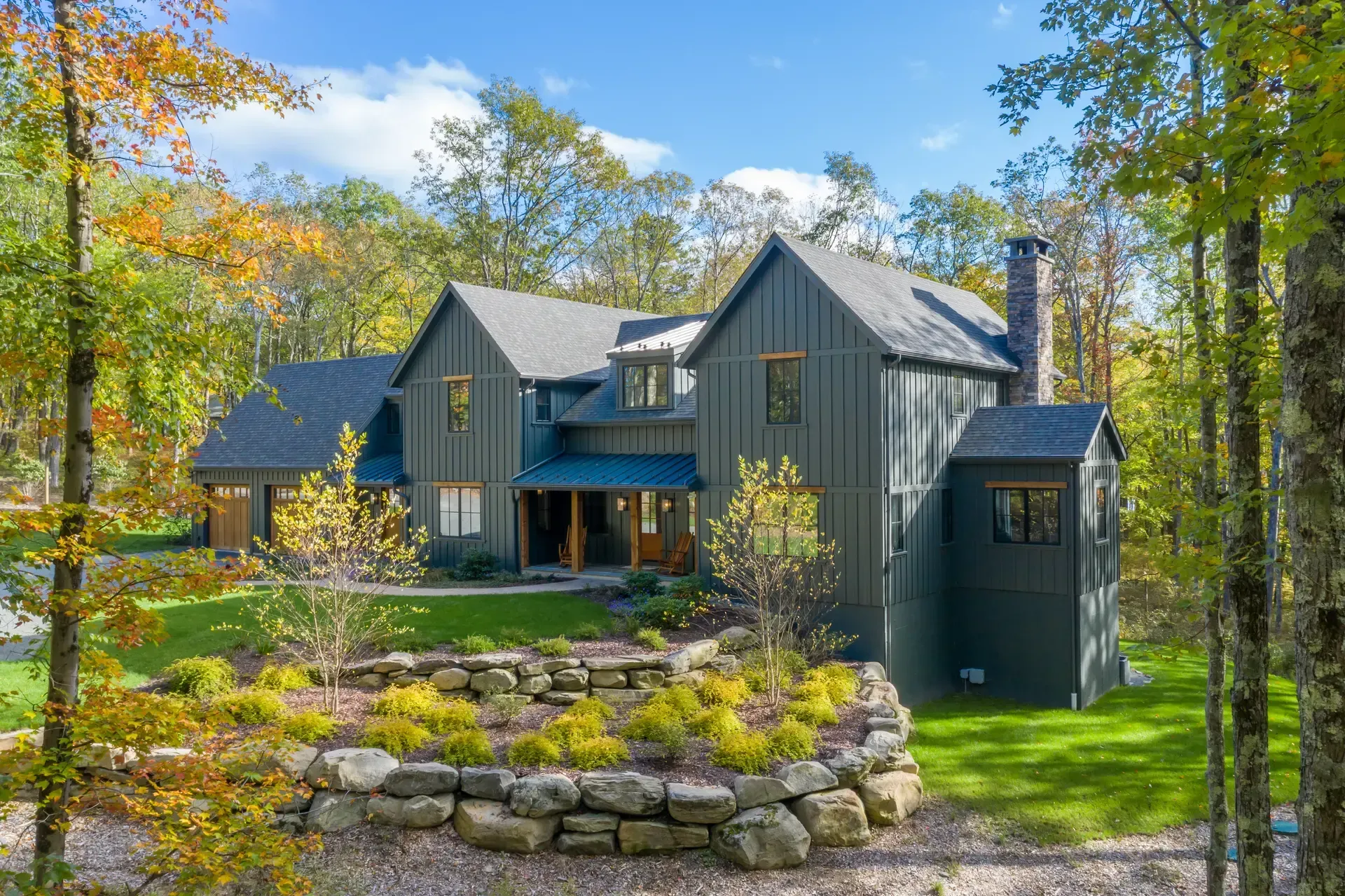 Gray house with blue trim nestled among autumn trees and stone landscaping