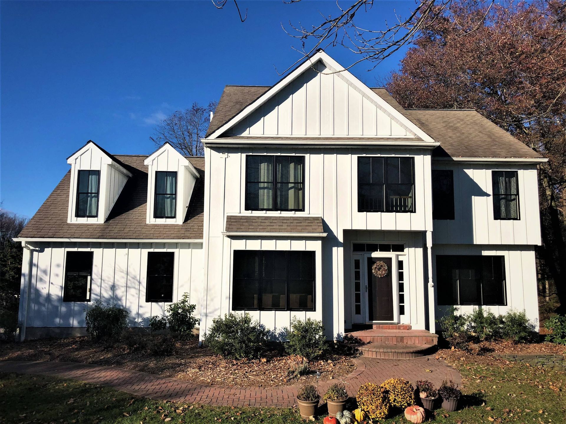 White two-story house with black shutters, front porch, and landscaped yard under a blue sky