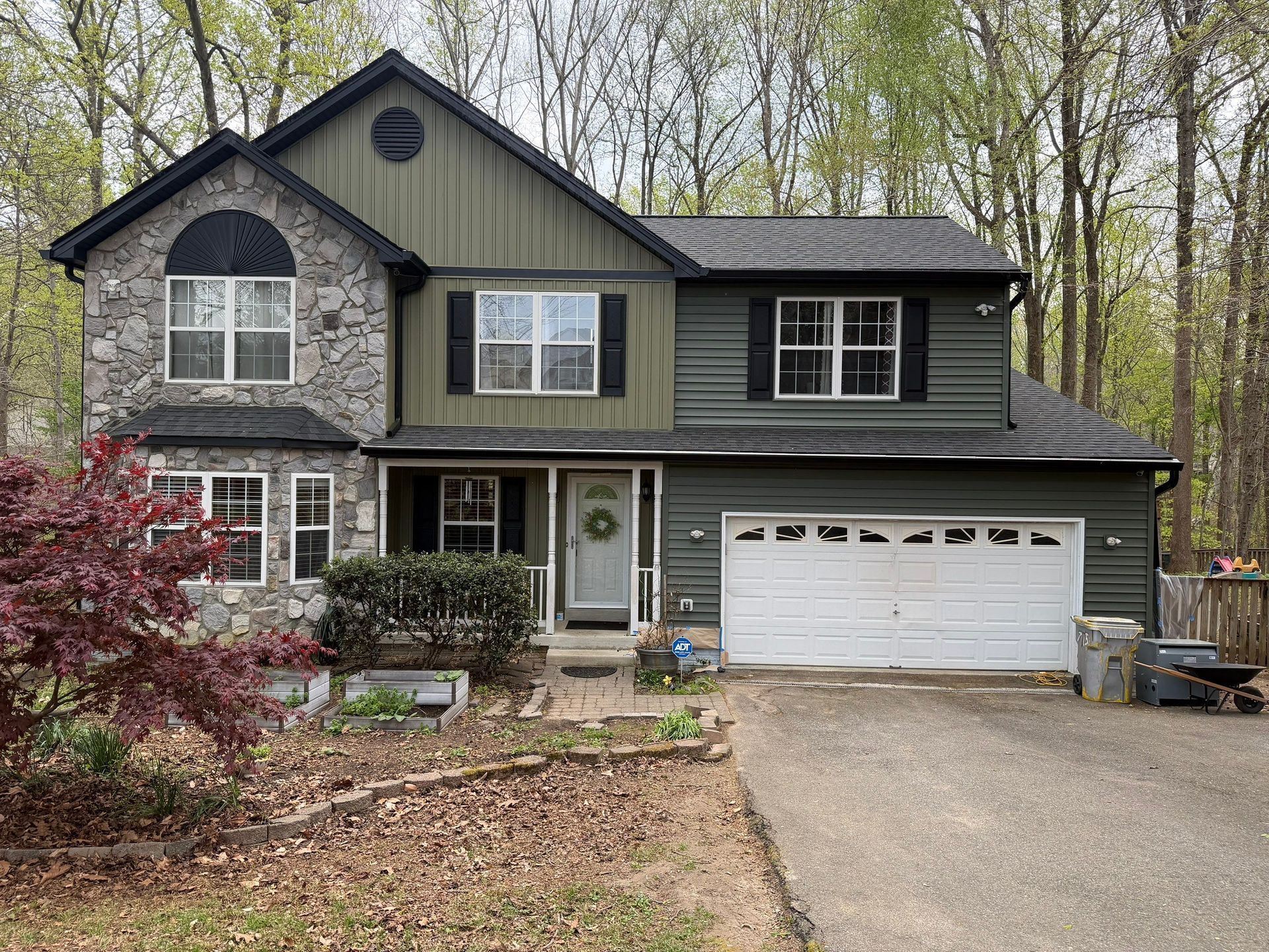 Two-story suburban house with stone and siding exterior, attached garage, and a driveway in a wooded setting