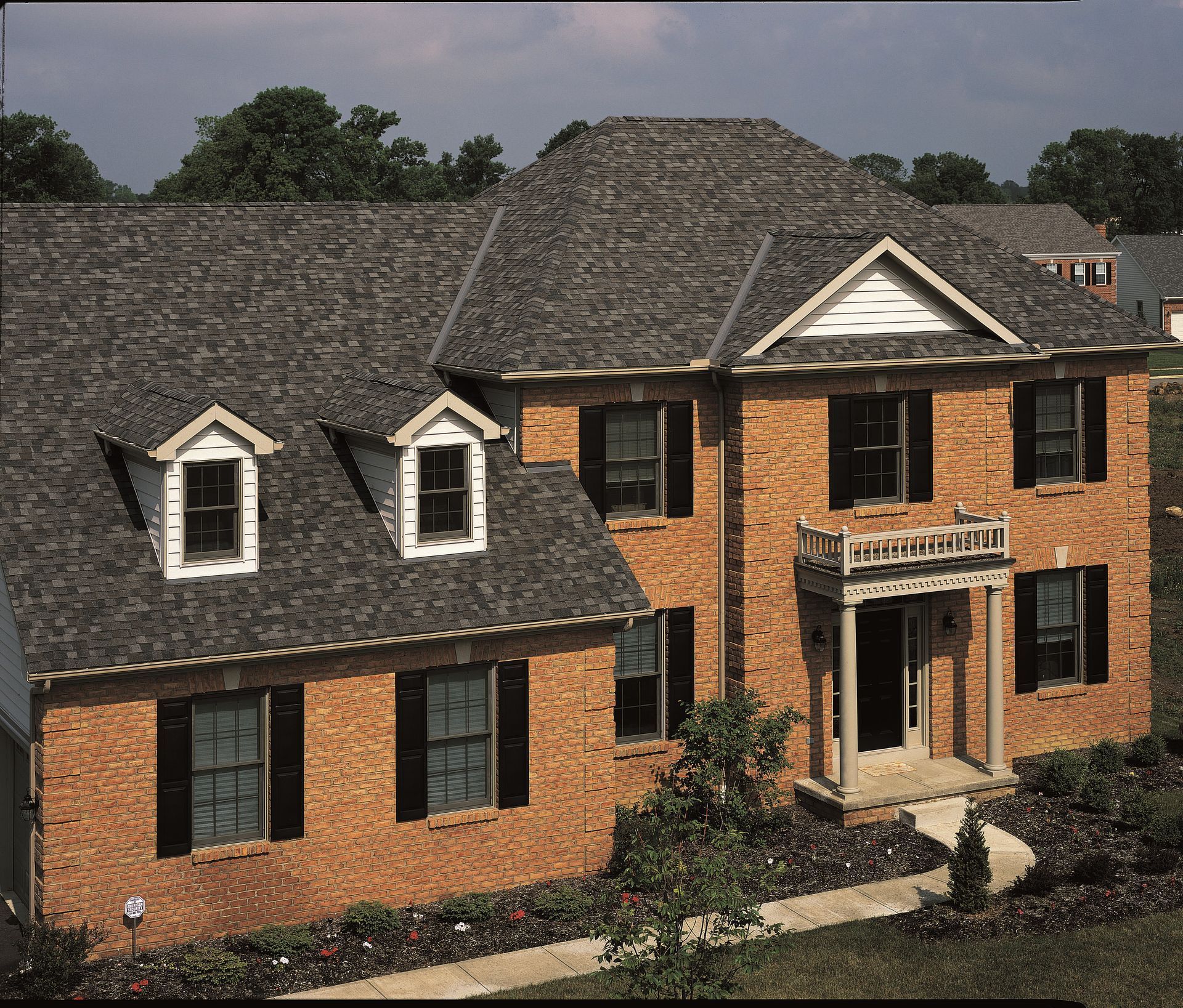 Large brick house with dark shingled roof, white-trimmed windows, and a front porch.