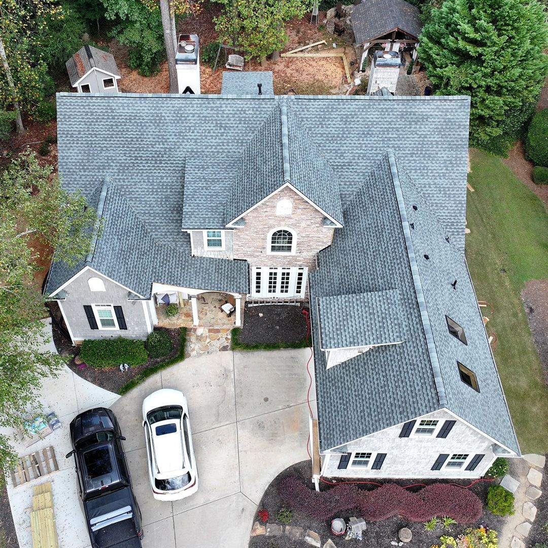 Aerial view of a gray-roofed suburban house with a curved driveway and parked cars.