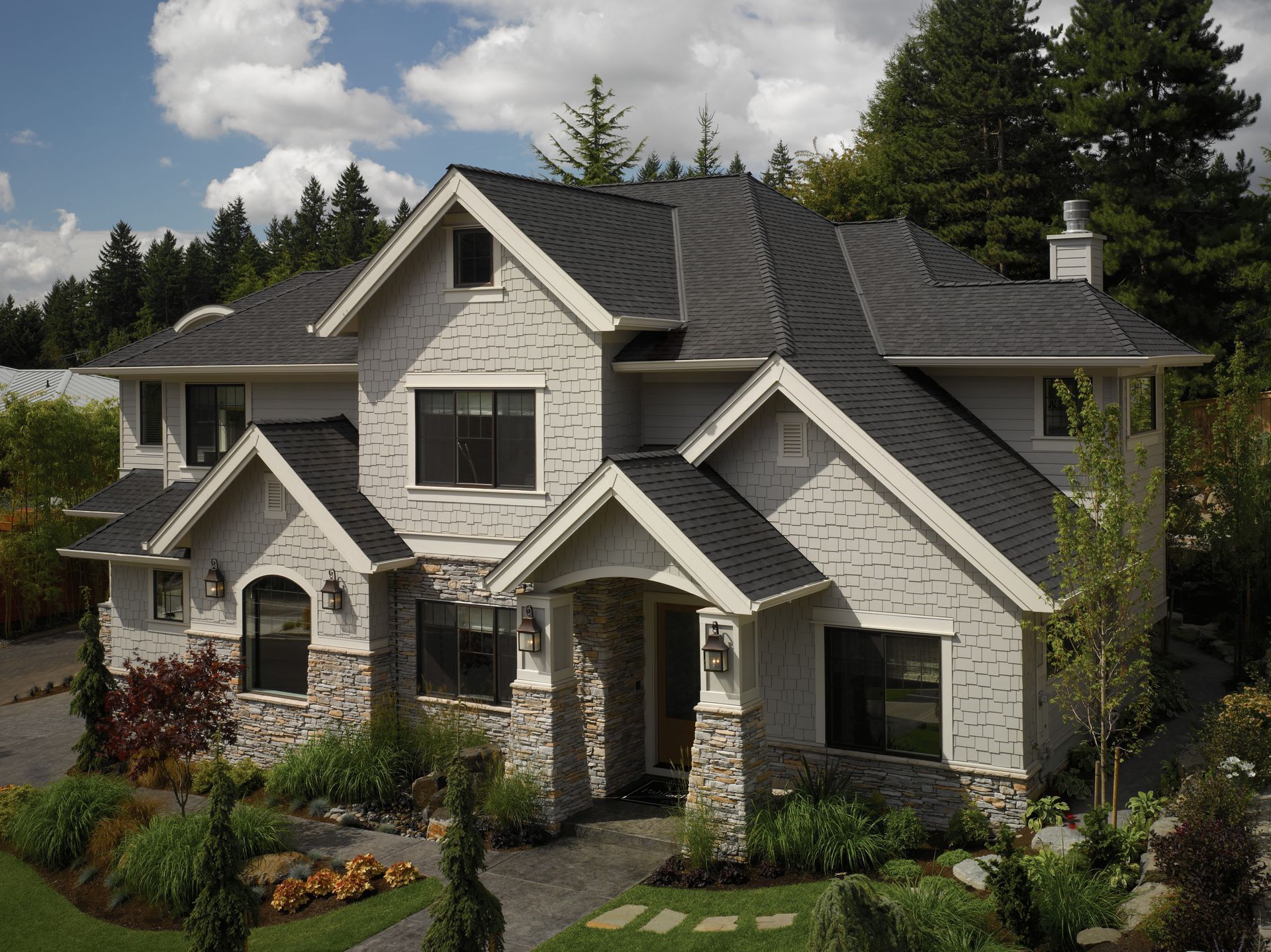 Large two-story gray stone house with multiple gables and a landscaped front yard