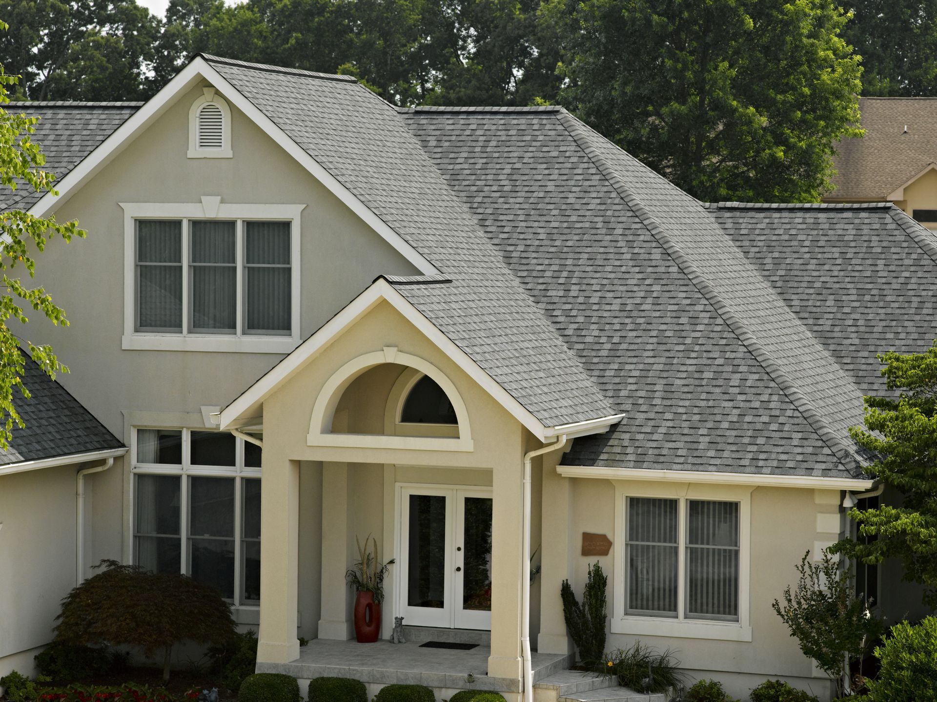 Suburban house with gray shingled roof, cream exterior, and front porch surrounded by trees