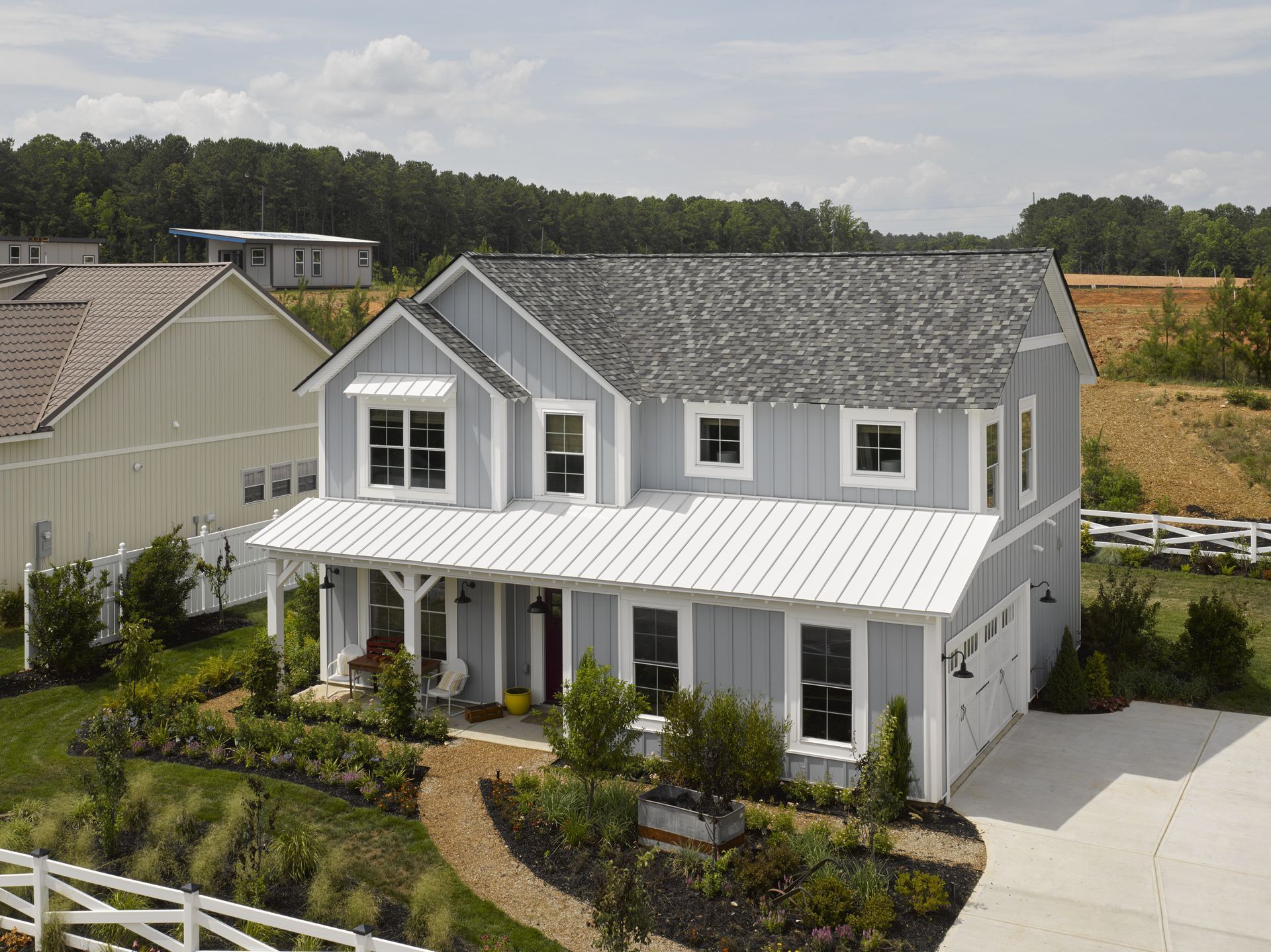 White two-story house with gray roof, front porch, and landscaped yard under a partly cloudy sky
