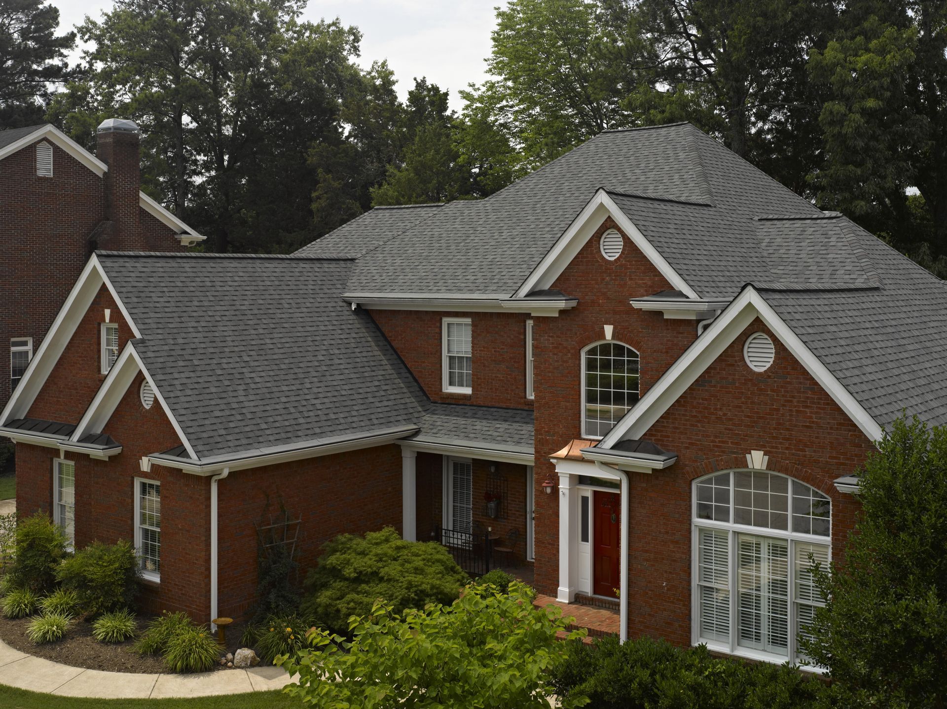 Brick suburban house with dark gray roof, white trim, and landscaped front yard